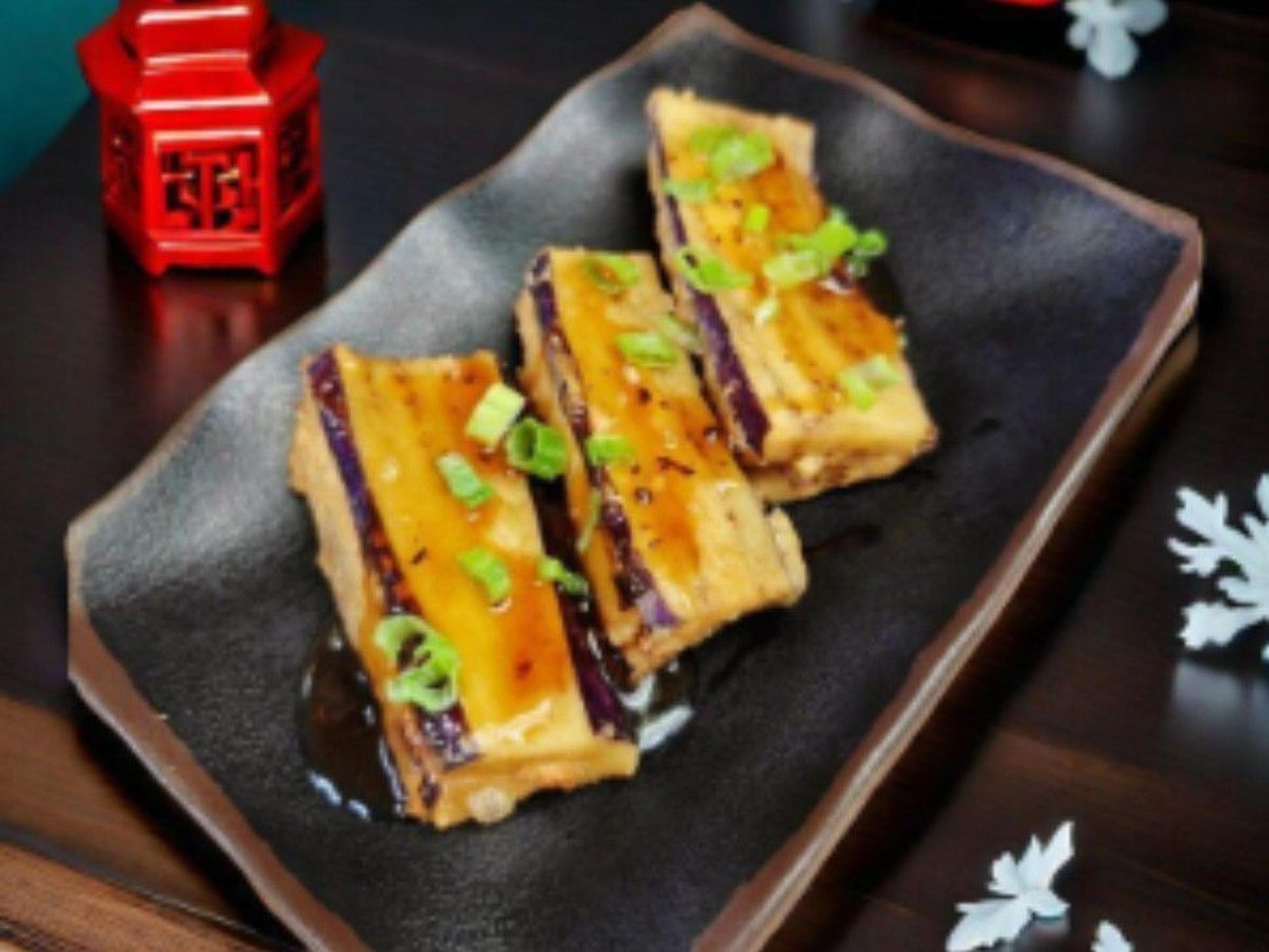 Slices of grilled tofu garnished with chopped green onions on a black plate