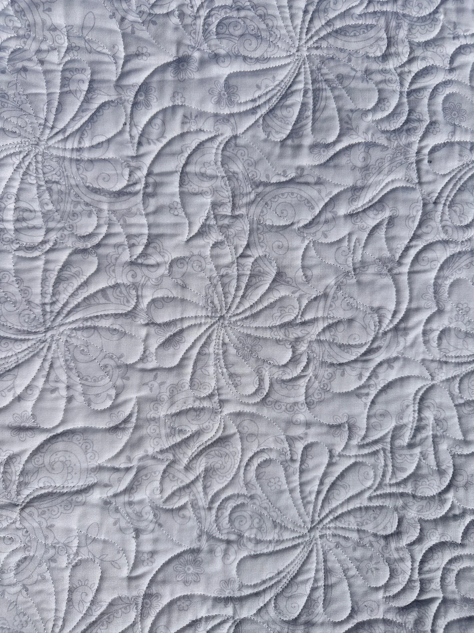 Close-up of a detailed white quilt with intricate floral and swirl stitching patterns.