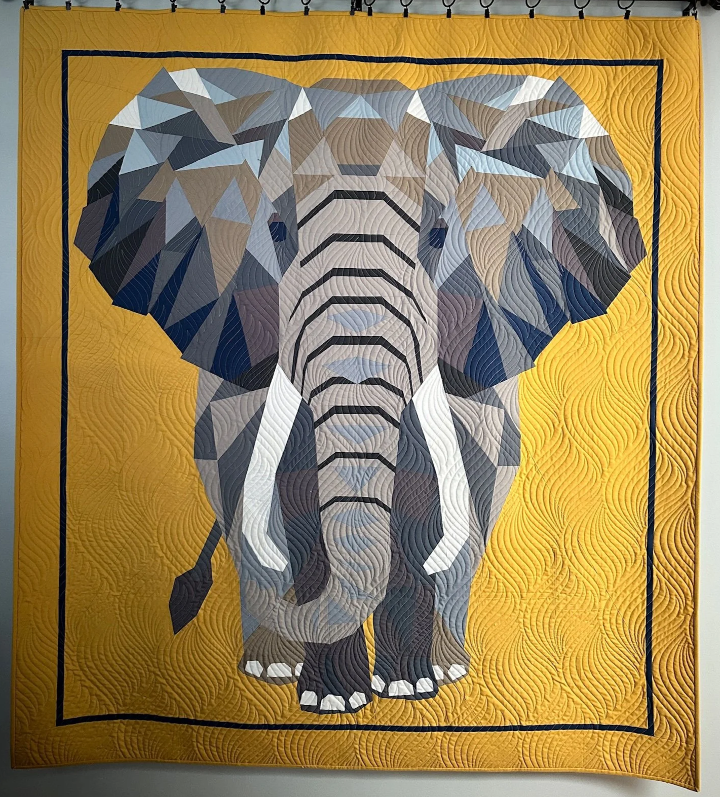 A patchwork quilt featuring a geometric, stylized elephant head design on a yellow background.