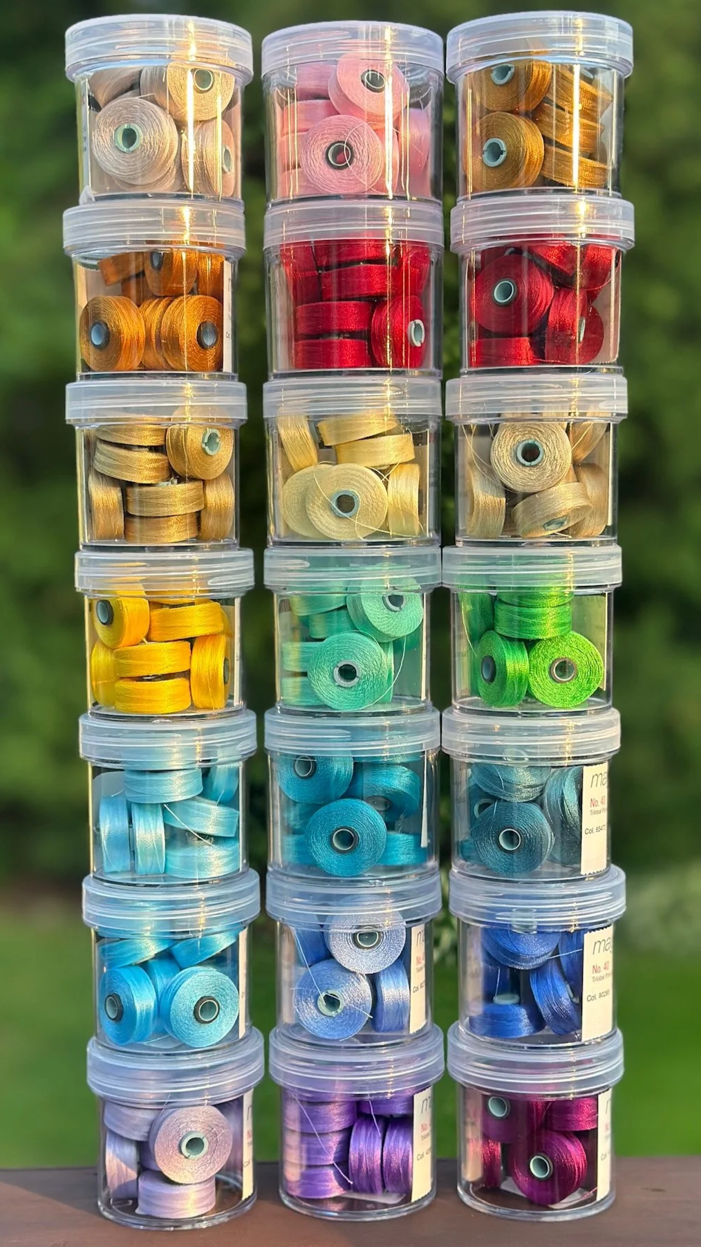 Stacked small transparent plastic containers filled with colorful quilting thread bobbins arranged by color. Used in longarm quilting service in Marblehead MA