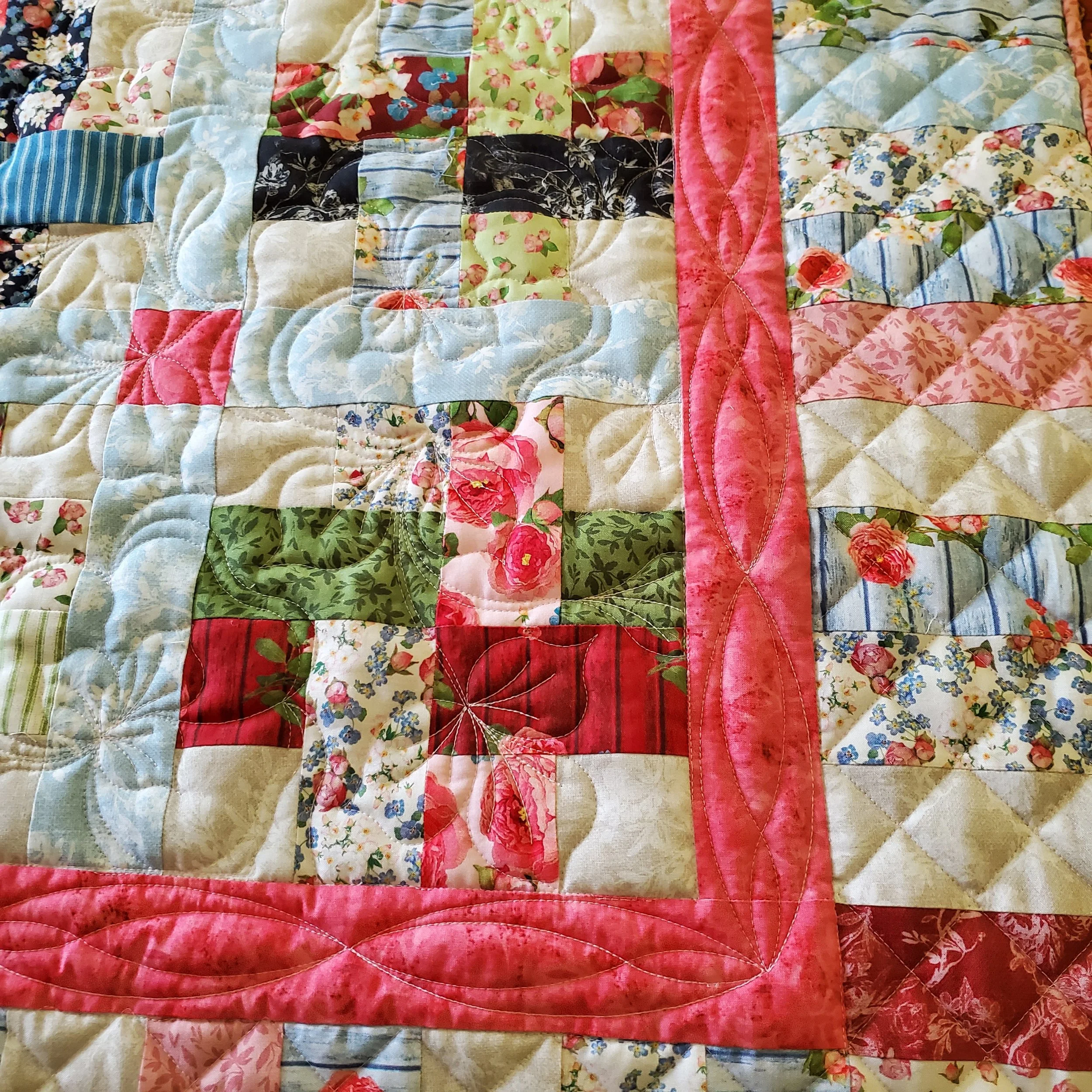 Close-up view of a colorful quilt with various floral and striped fabric patterns, stitched together in a patchwork design.