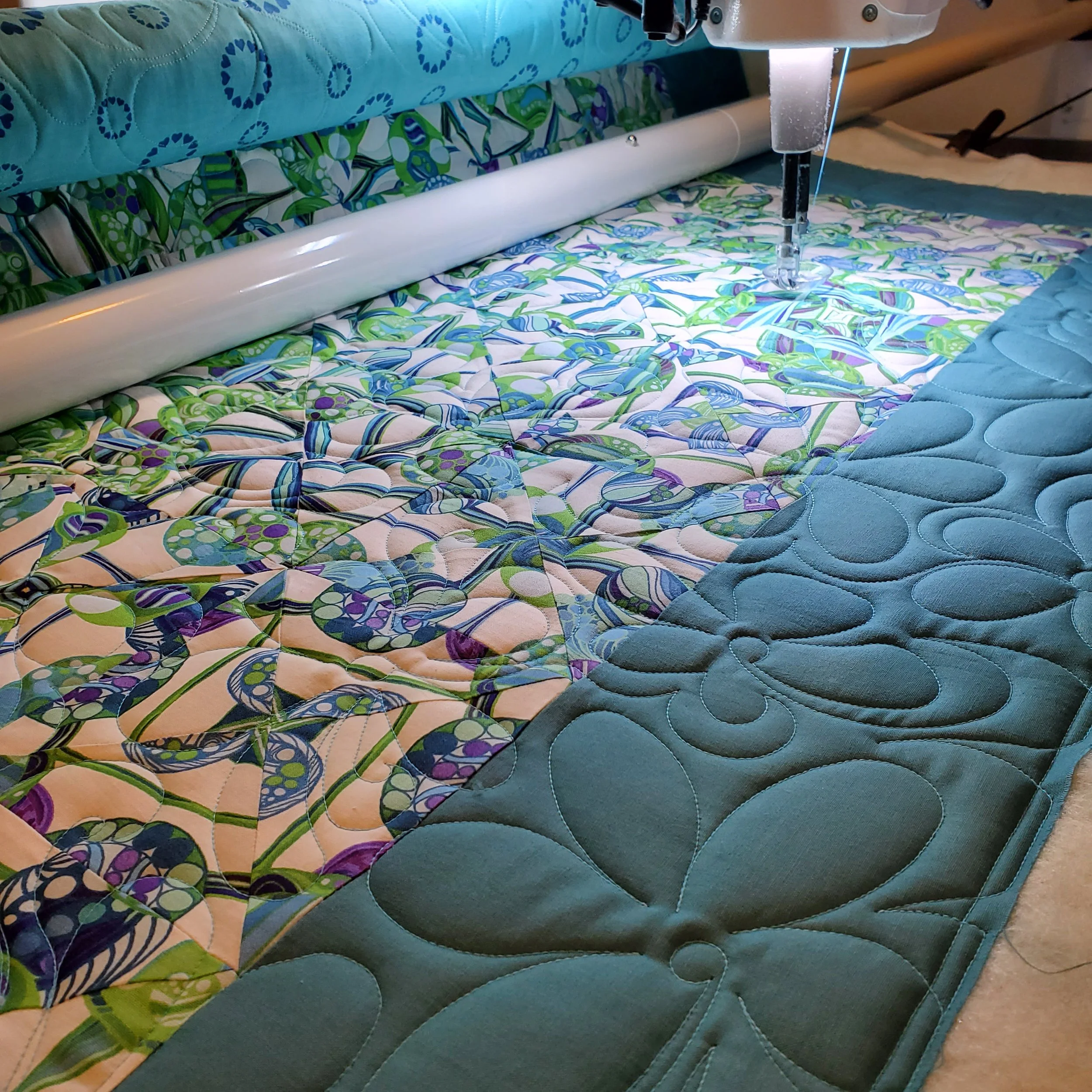 Close-up of a sewing machine stitching a colorful quilt with floral and abstract patterns, set on a table.
