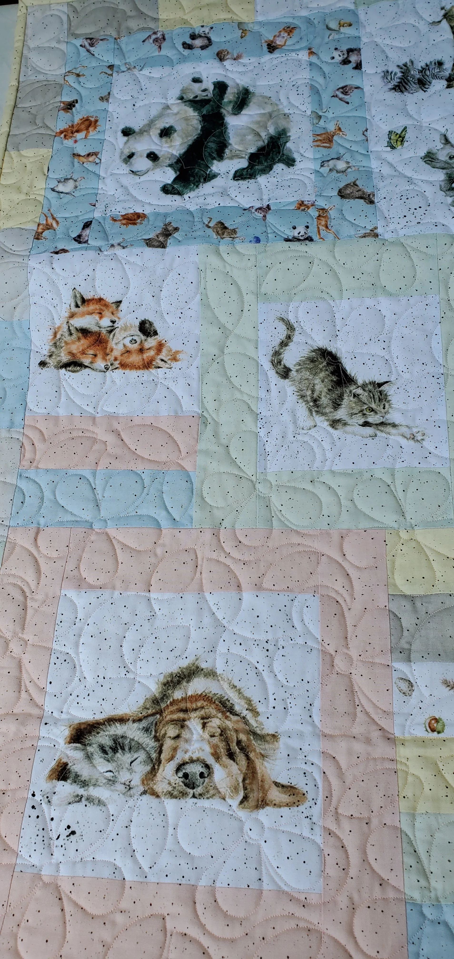 A colorful quilt with pictures of animals, including pandas, foxes, cats, wolves, and a lion, arranged in squares.