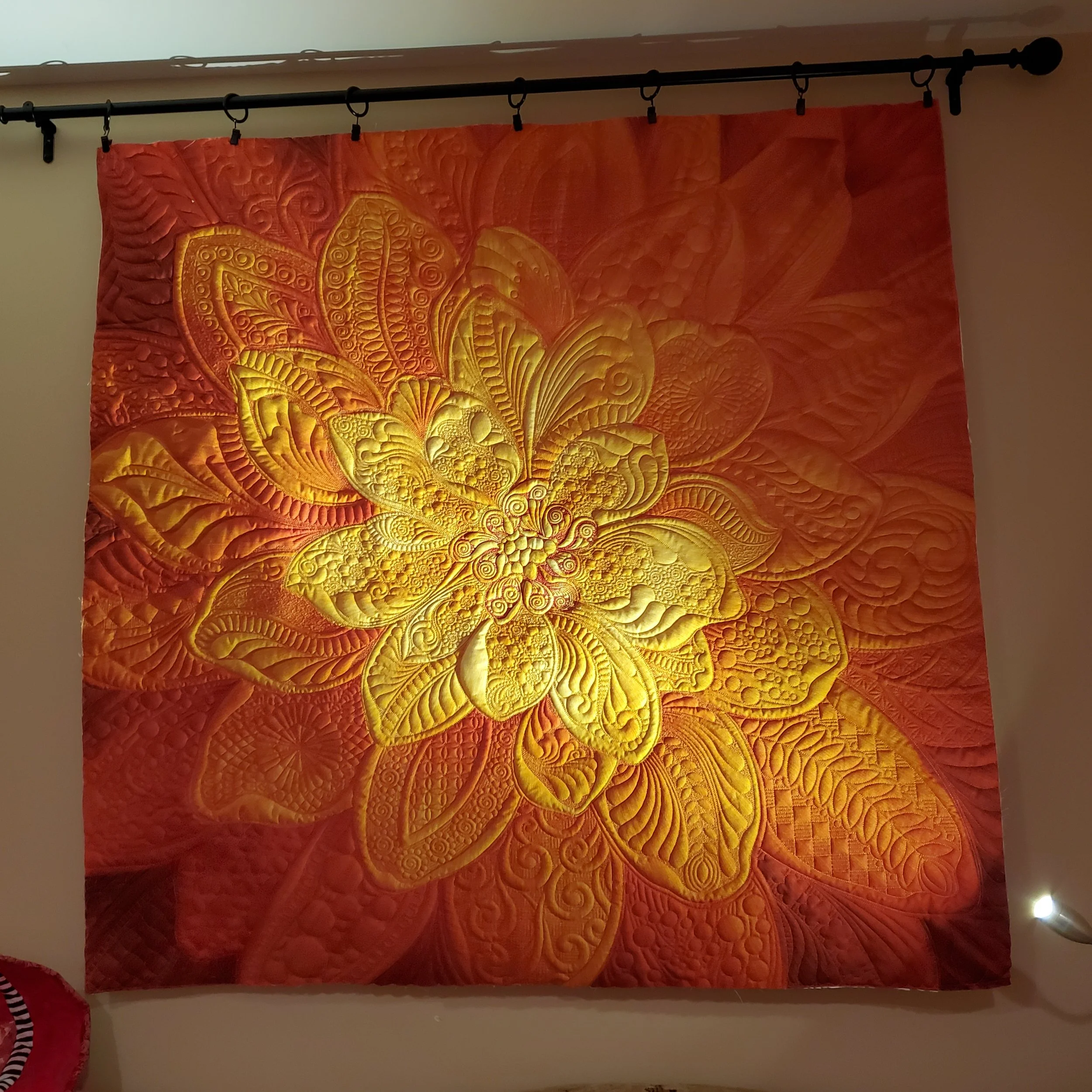 A quilt with orange and yellow patterns hanging on a wall.