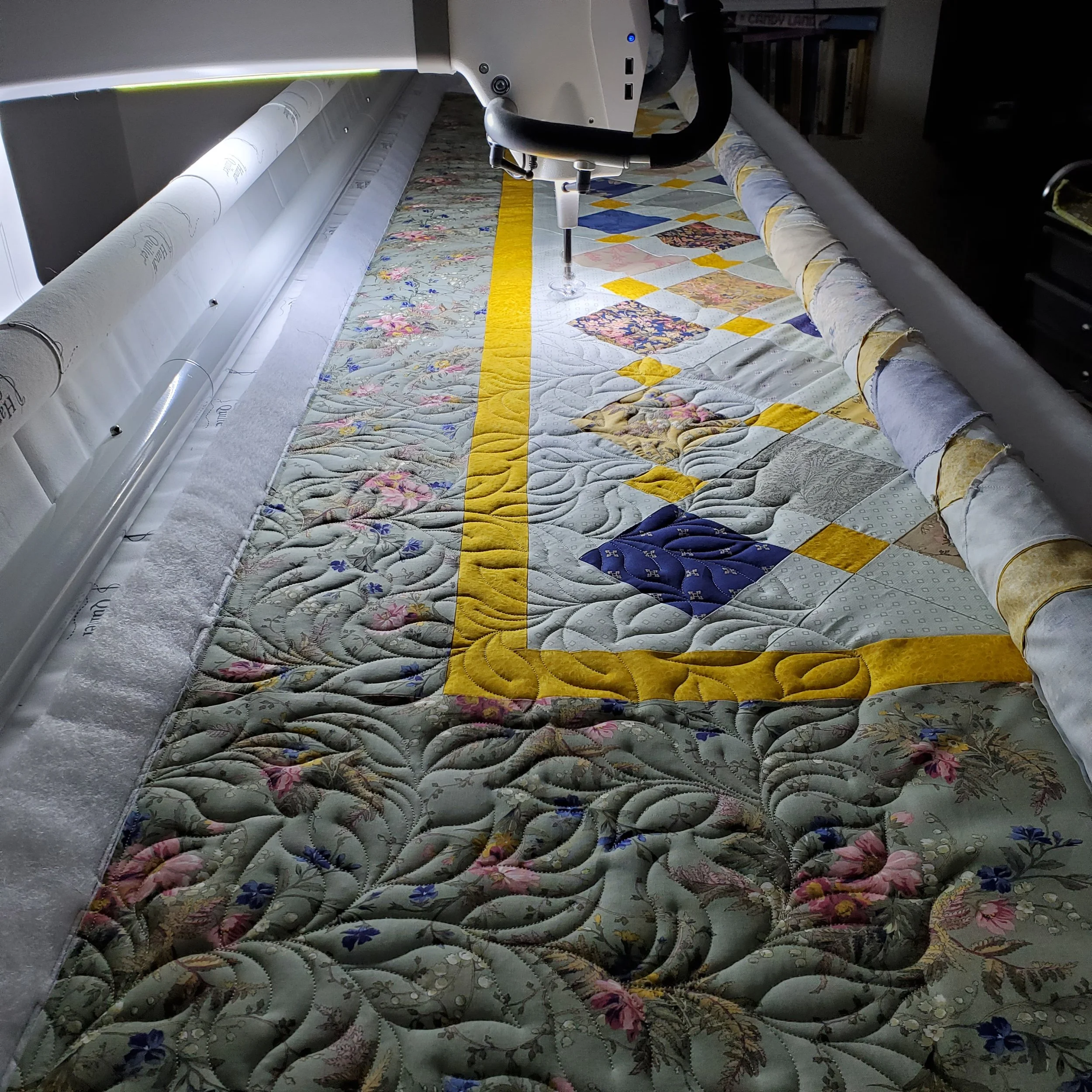 A computerized longarm quilting machine sewing a floral quilt with a yellow border.