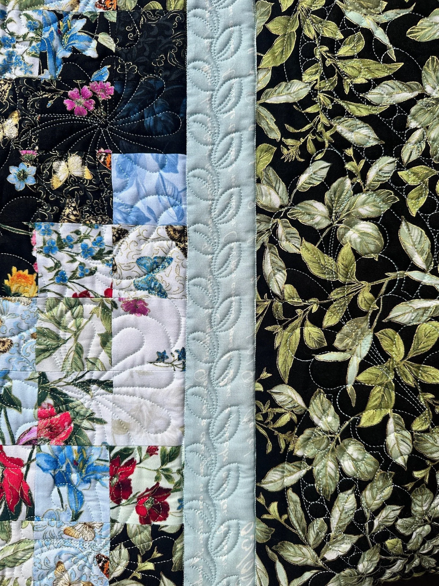 A close-up of a patchwork quilt with floral and leaf patterns, stitched with decorative quilting lines, long arm quilted in Marblehead MAquilted