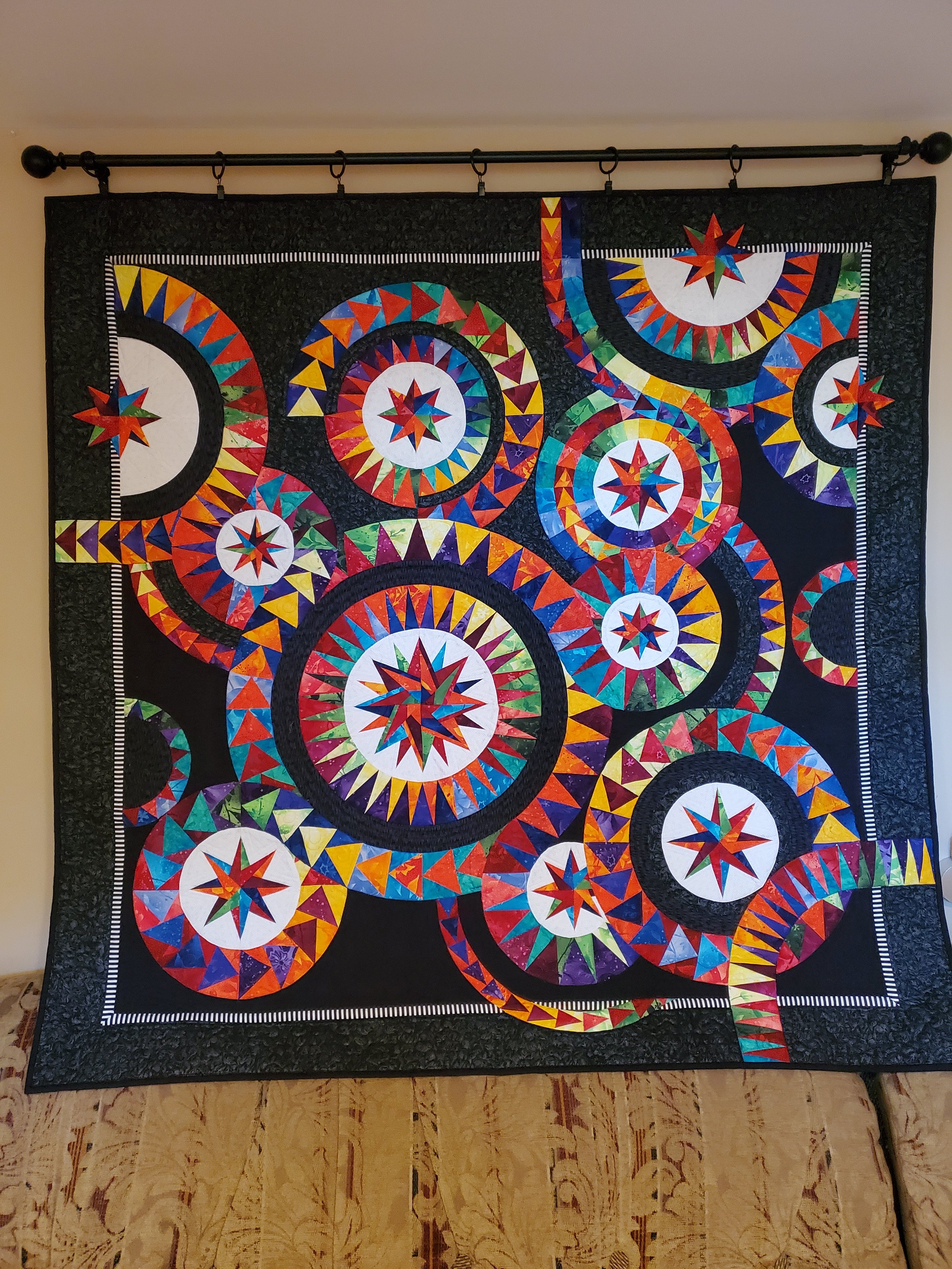 Colorful geometric quilt with circular and star patterns hanging on a black background wall