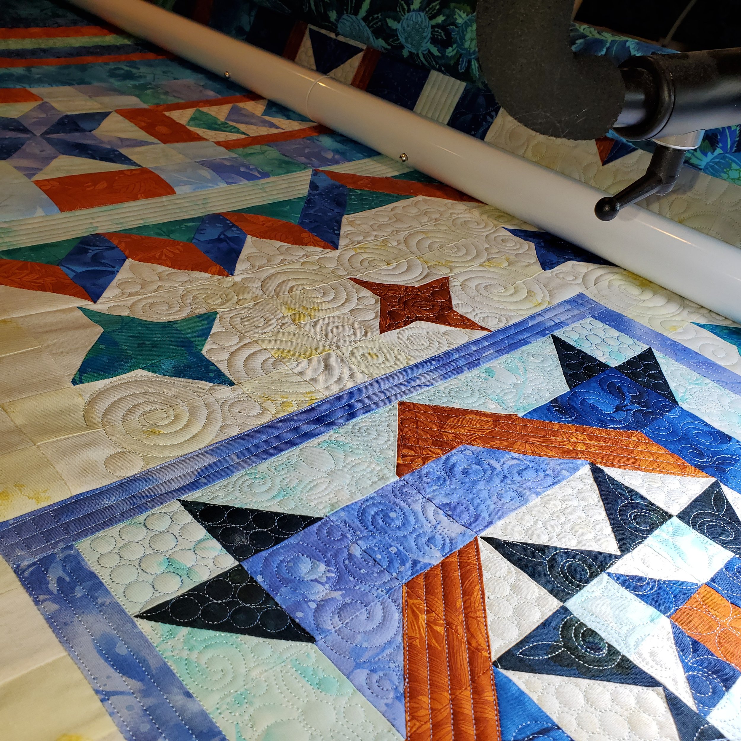 Close-up view of a colorful quilt on a bed, with a black cylindrical object and a white pole across the quilt.