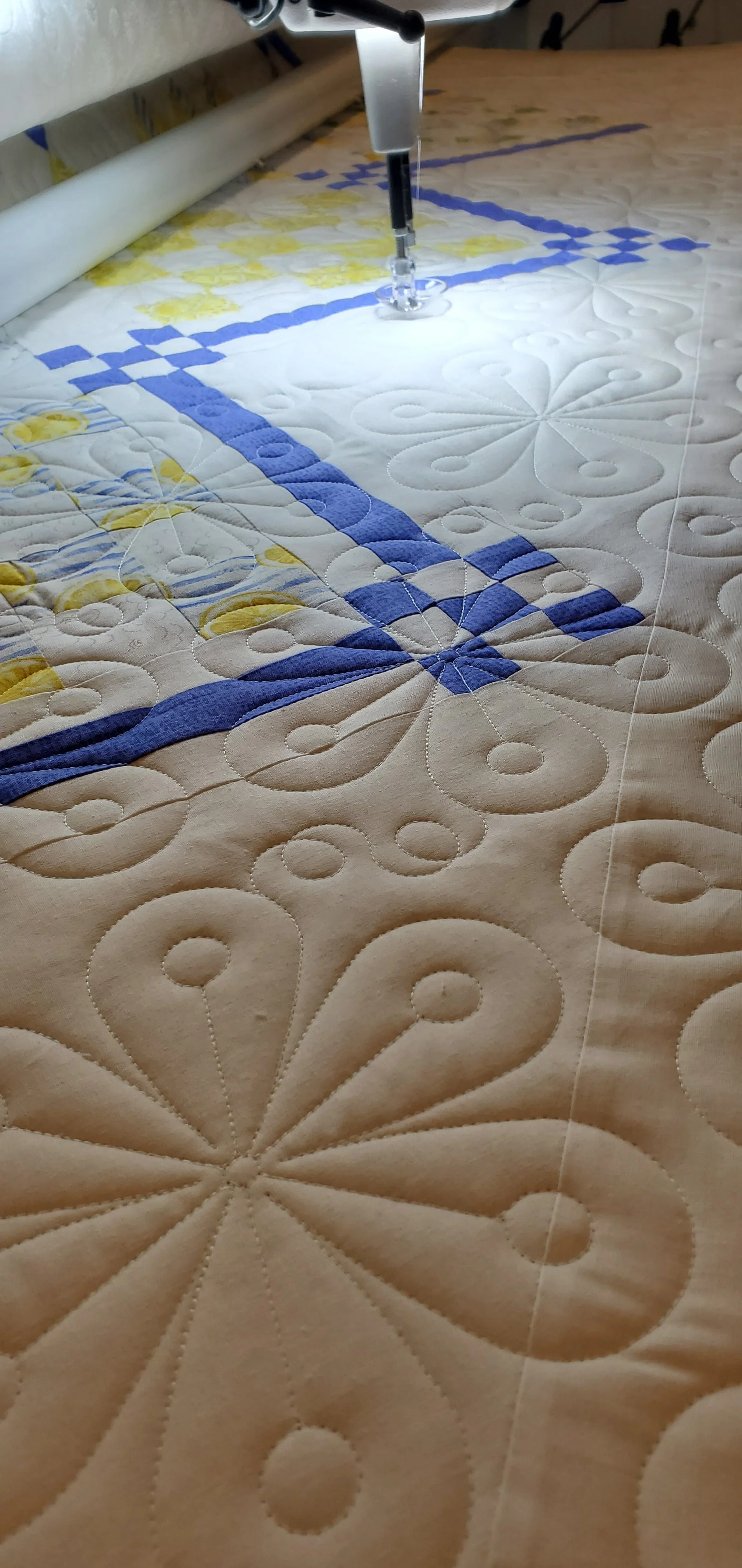Close-up of a sewing machine quilting a beige, floral and geometric patterned fabric with blue and yellow accents.