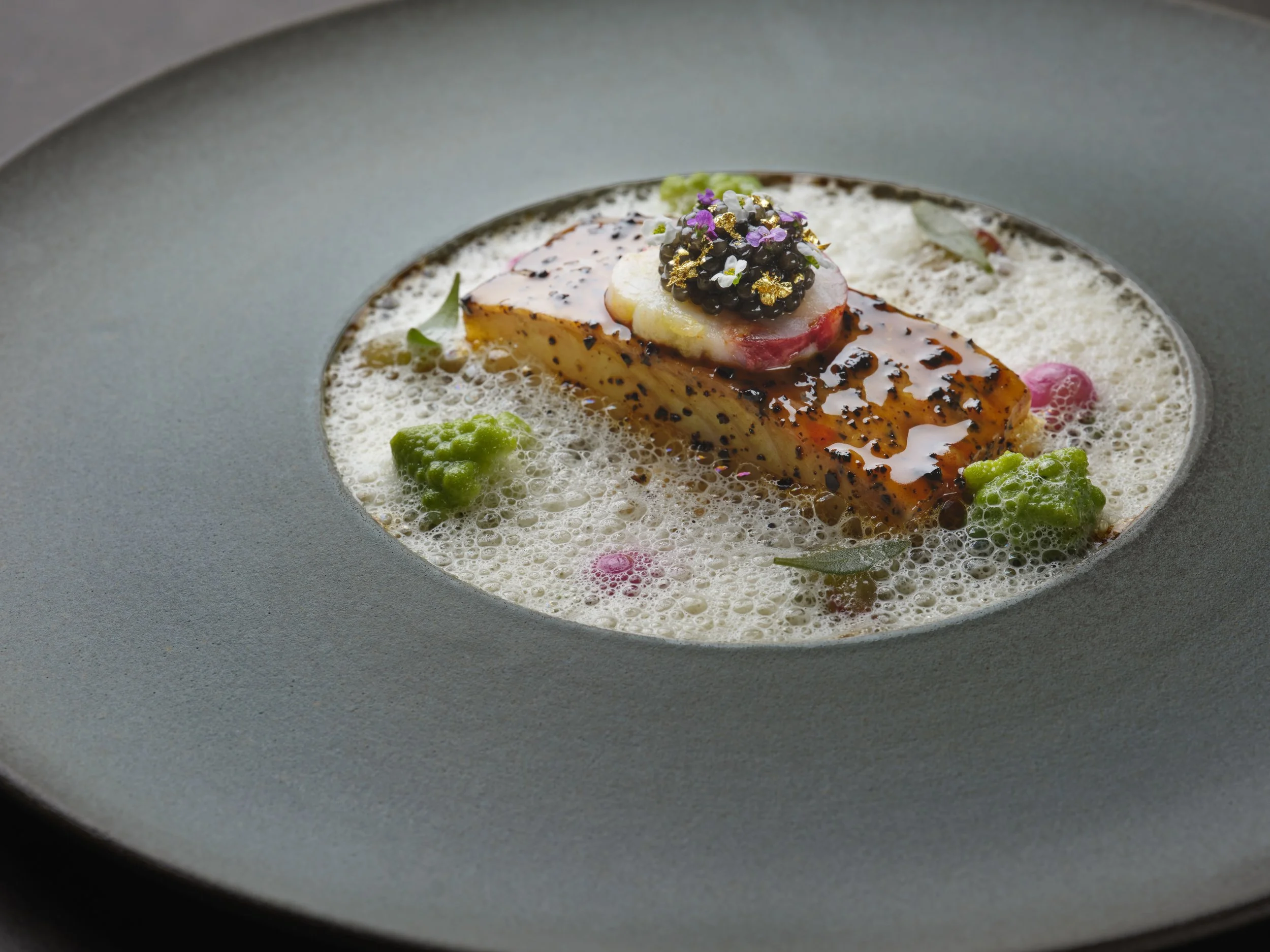 Close-up of a plated gourmet dish featuring a piece of turbot, native lobster, caramelised cauliflower and salted grapes topped with caviar.