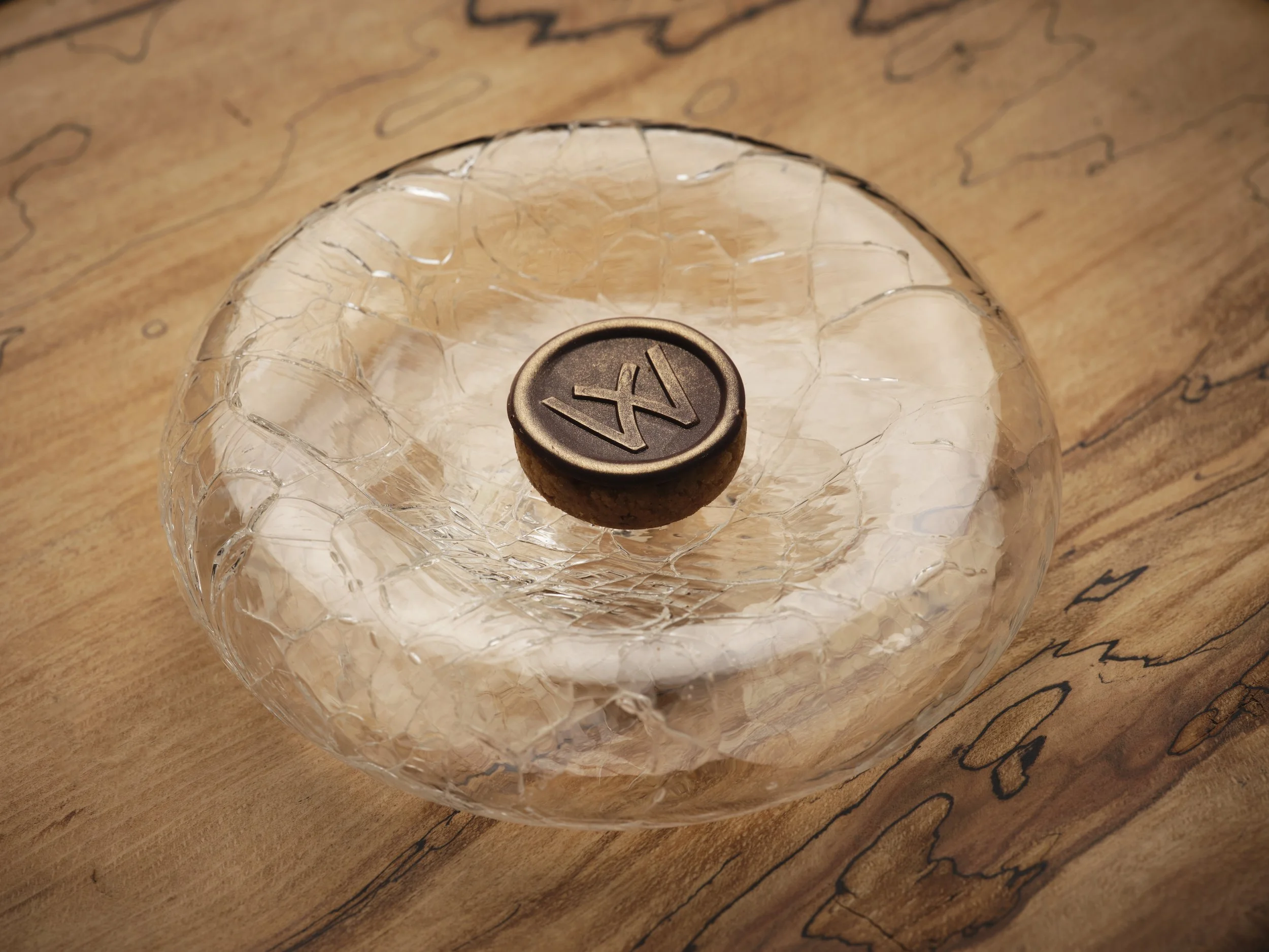 A clear glass with ice cubes sitting on a wooden surface, with a black corkscrew on top of the ice cubes.