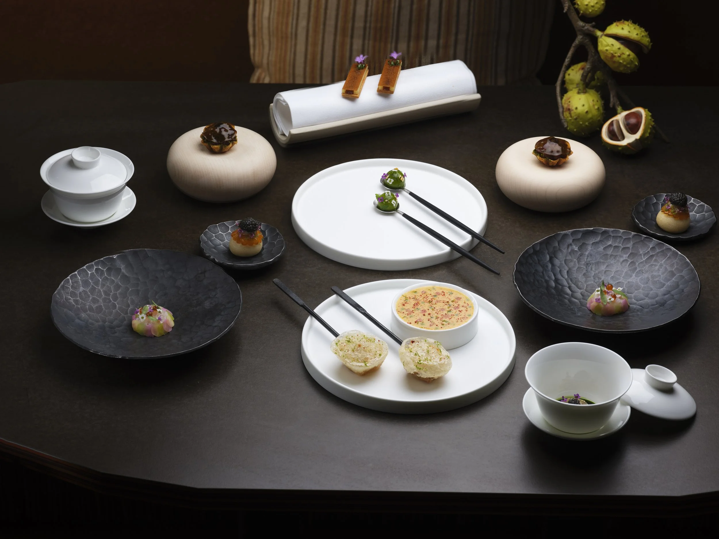 An elegant display of assorted Japanese cuisine with small plates of canapes, starters, and appetizers on a dark table, accented by decorative elements and a branch with green berries.