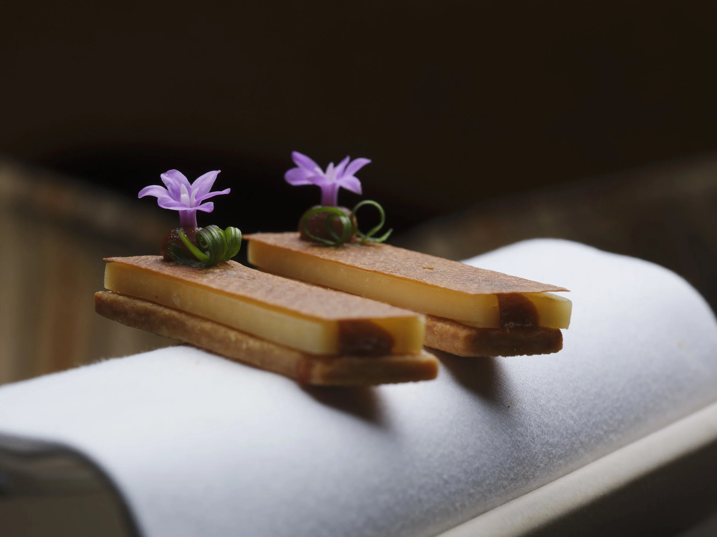 Close-up of layered cheese and onion sandwich snack with purple flowers and green garnish on top, on a white plate.