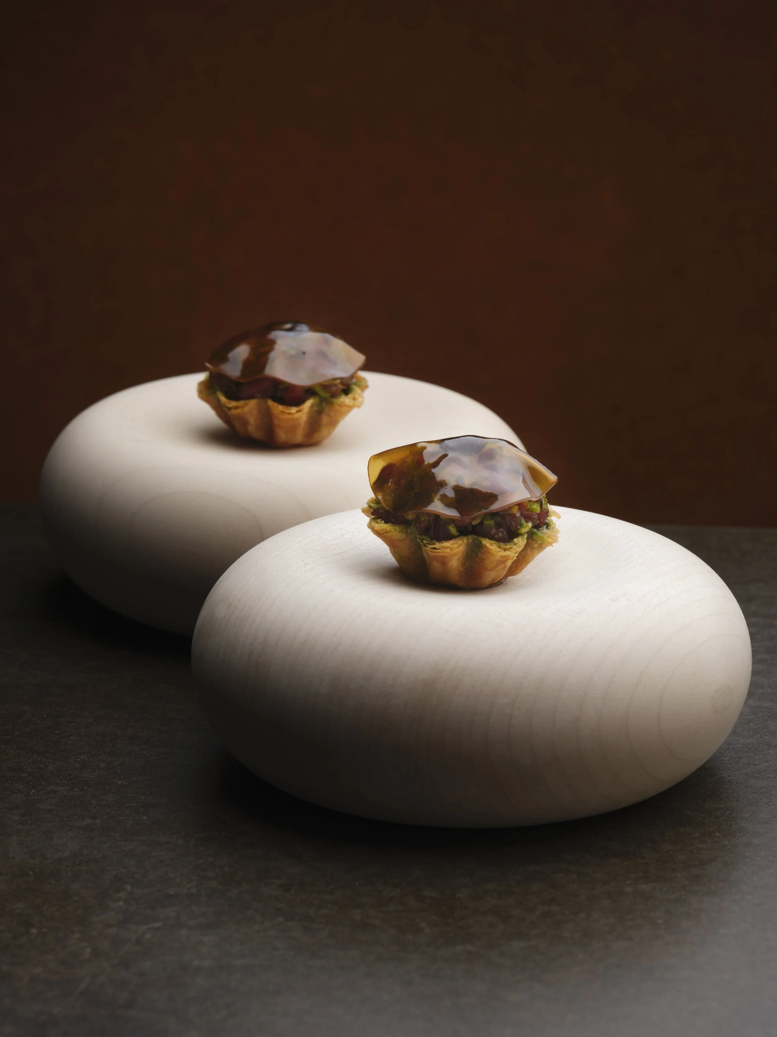 Two small appetizers with a spoonful of dark sauce on top, served on smooth, white, rounded stones as a presentation plate.