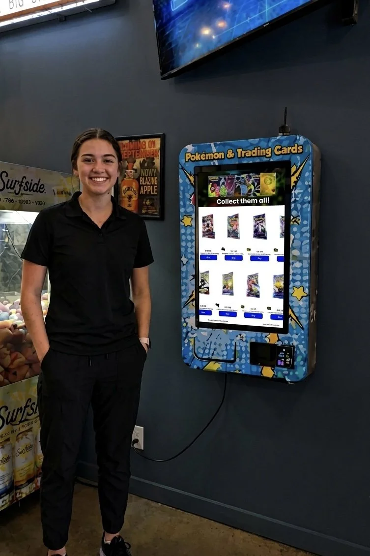 A young woman smiling and standing next to a digital screen vending machine for Pokemon trading cards in a store.