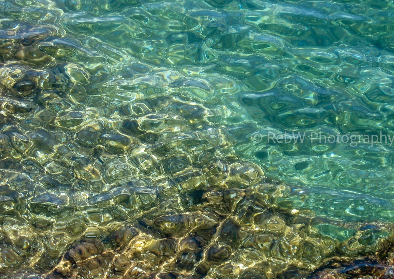 The sun bounces off the cool blue-green waters of the Adriatic. Rocks can be seen through the water.