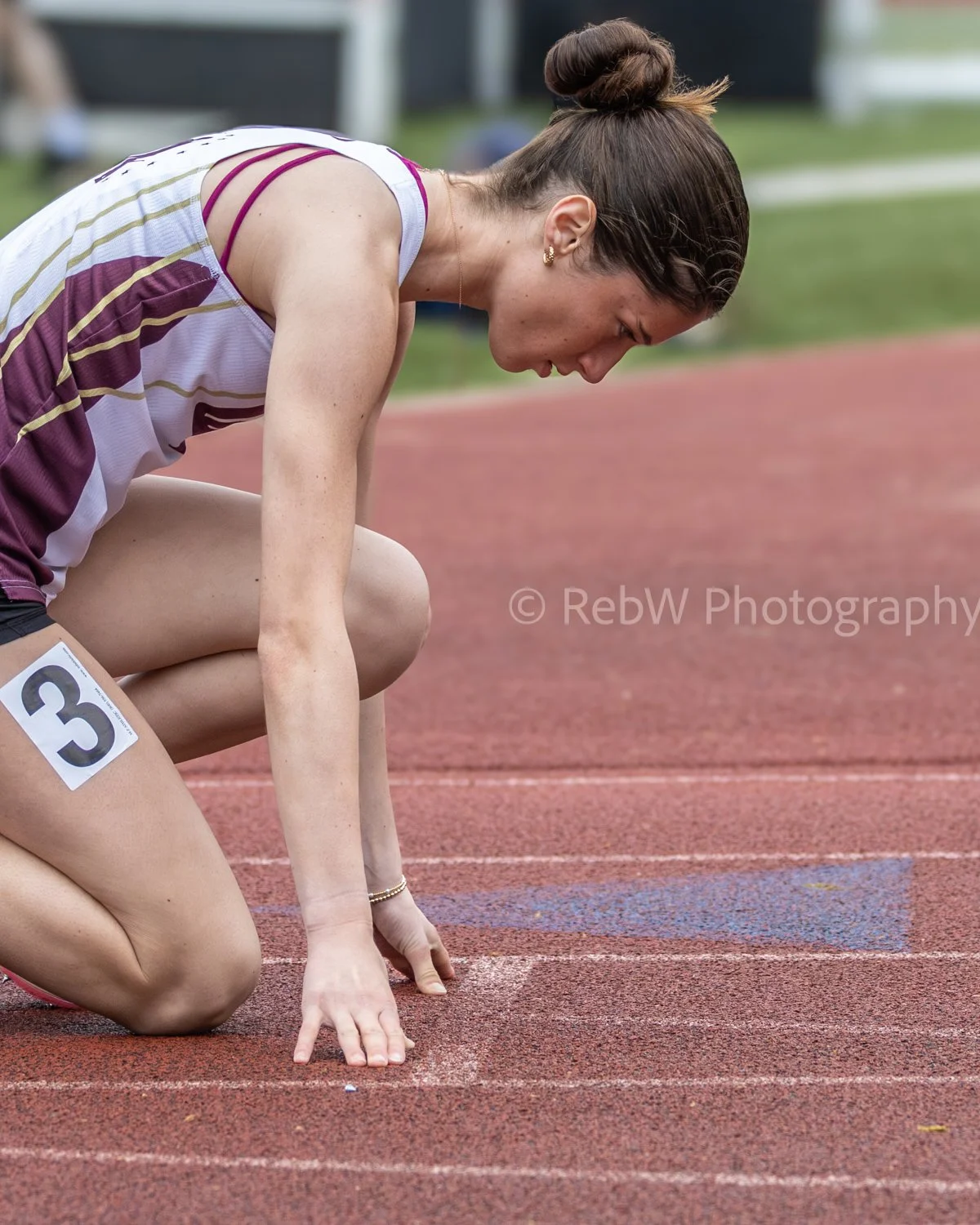 A female athlete in a sports uniform crouches on a running track at the starting line, preparing to race.