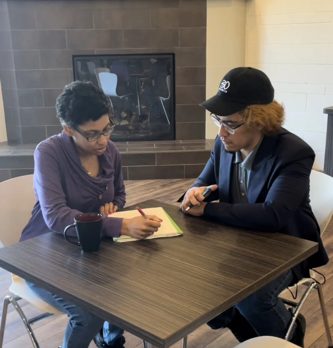 Two people seated at a table engaged in a discussion about the man's writing. The coach is providing feedback and critique.