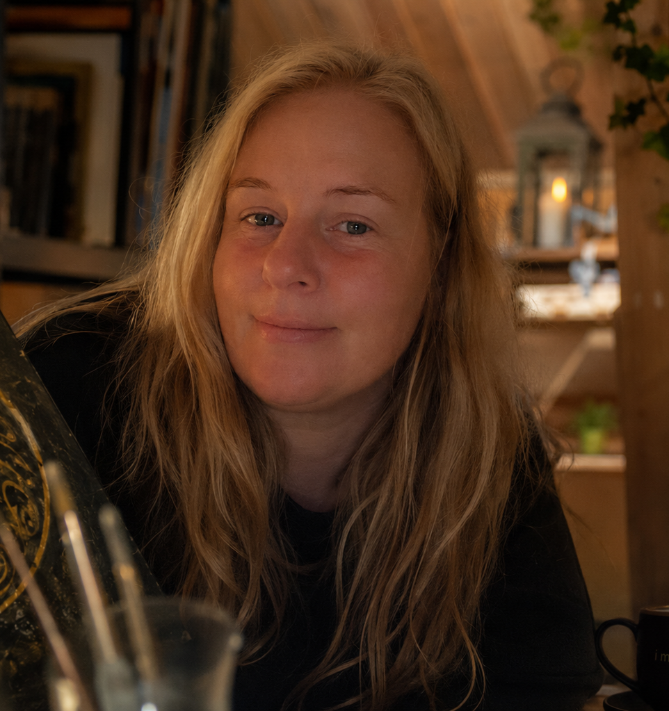 Portrait of the artist smiling in a warm, cosy interior with wooden shelves in the background.
