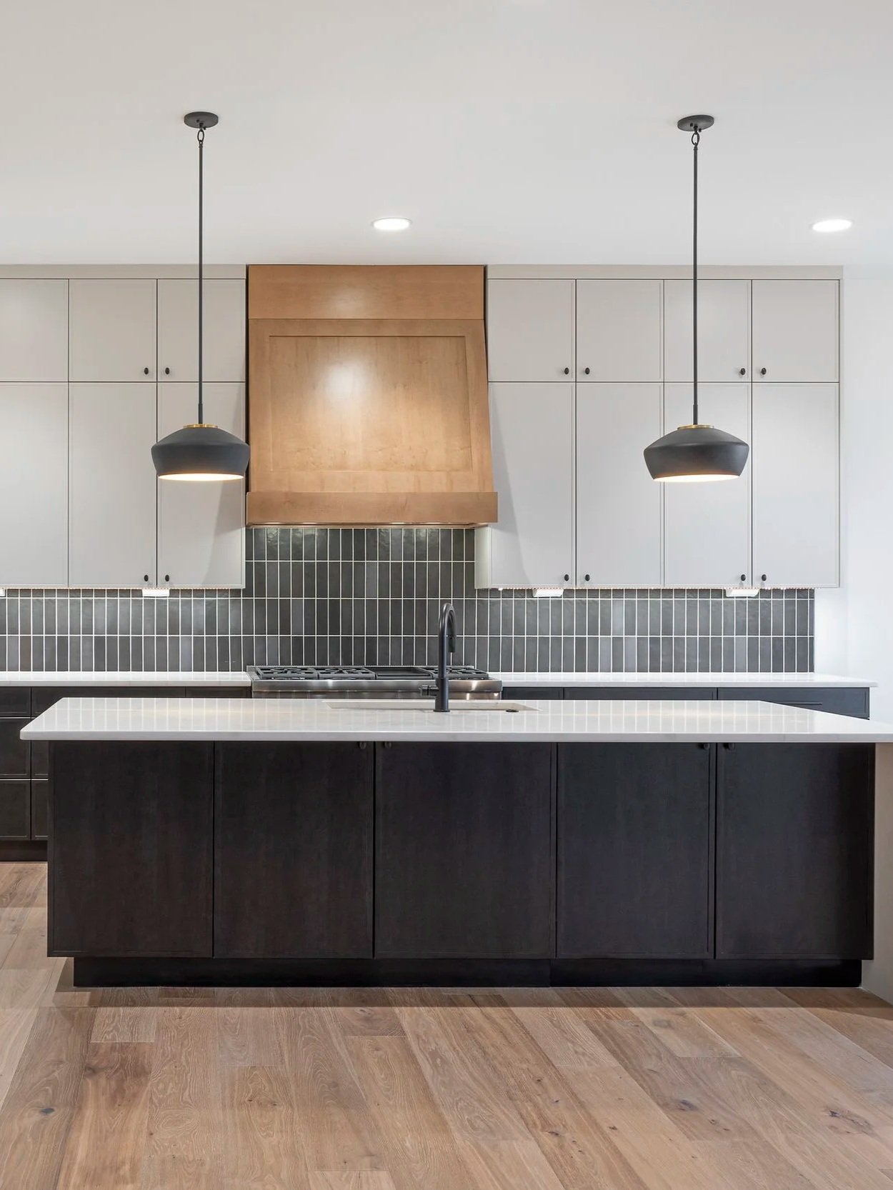 Modern yet classic kitchen design with wood hood range, large oversized kitchen island with pendant lights and dark gray subway tile