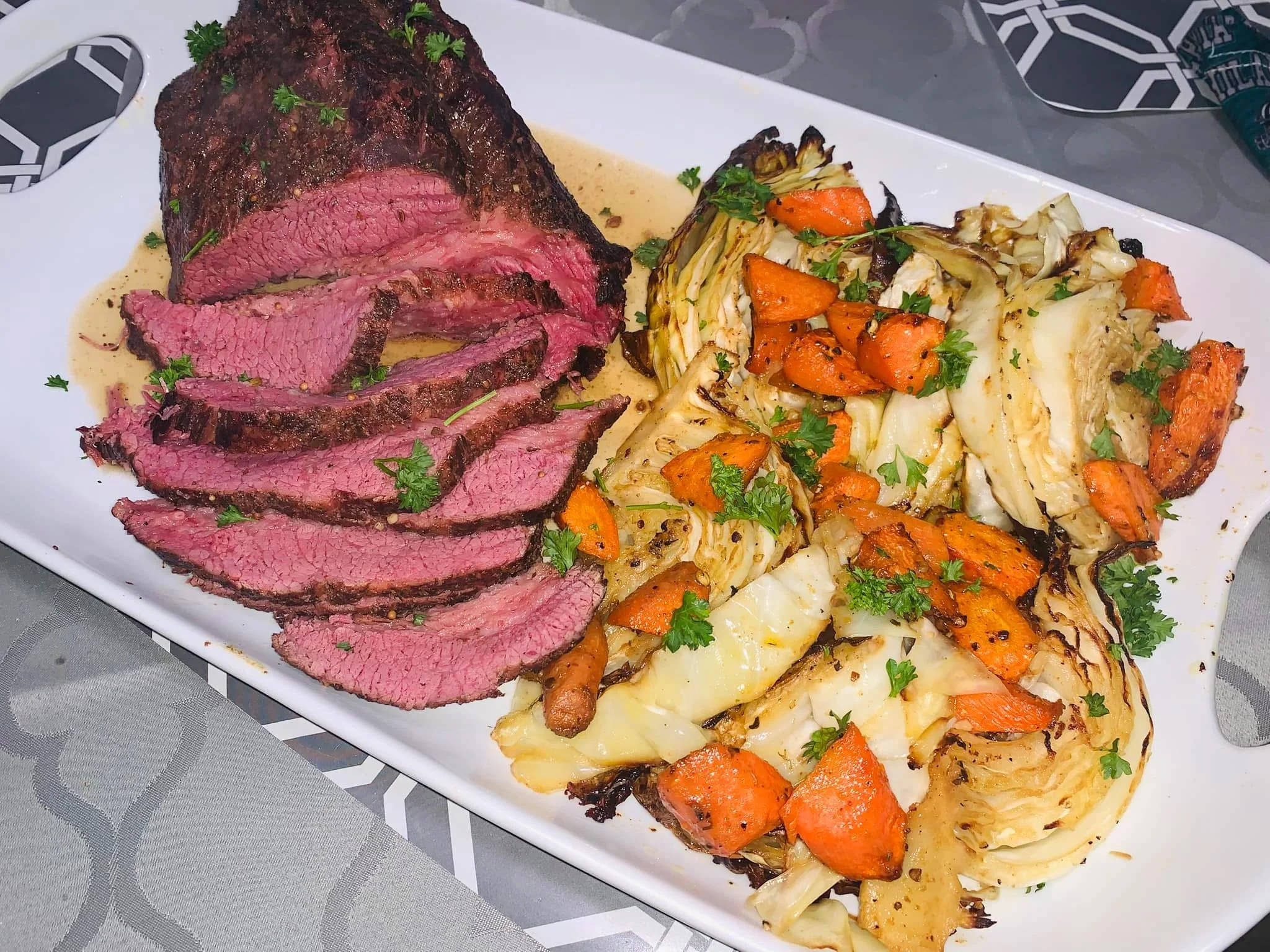 A white rectangular plate with sliced medium-rare steak and roasted vegetables, garnished with parsley.