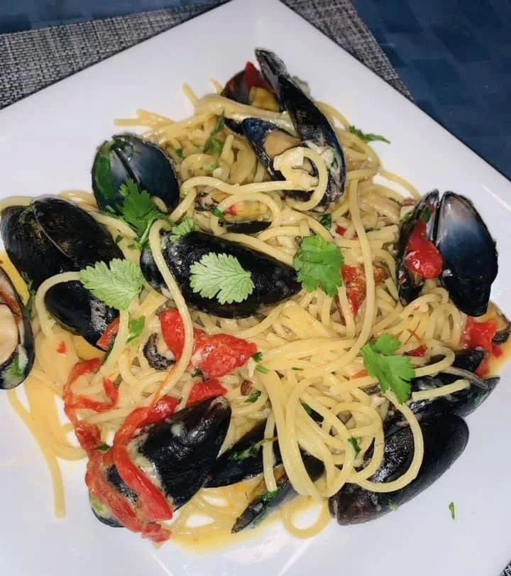 A plate of spaghetti with black mussels, chopped tomatoes, and cilantro garnished.