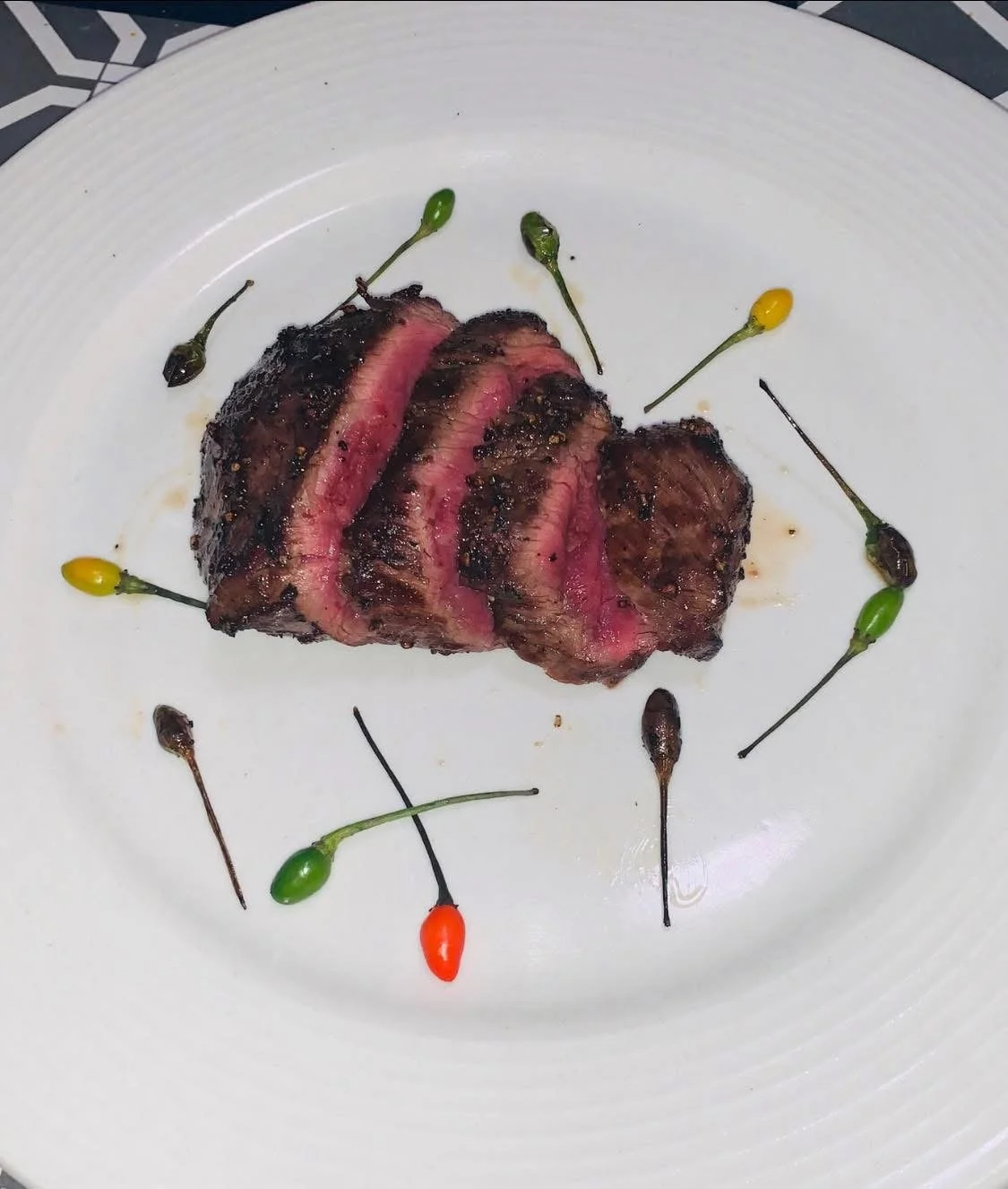 Slices of cooked steak with a pink center, garnished with colorful small peppers on a white plate.