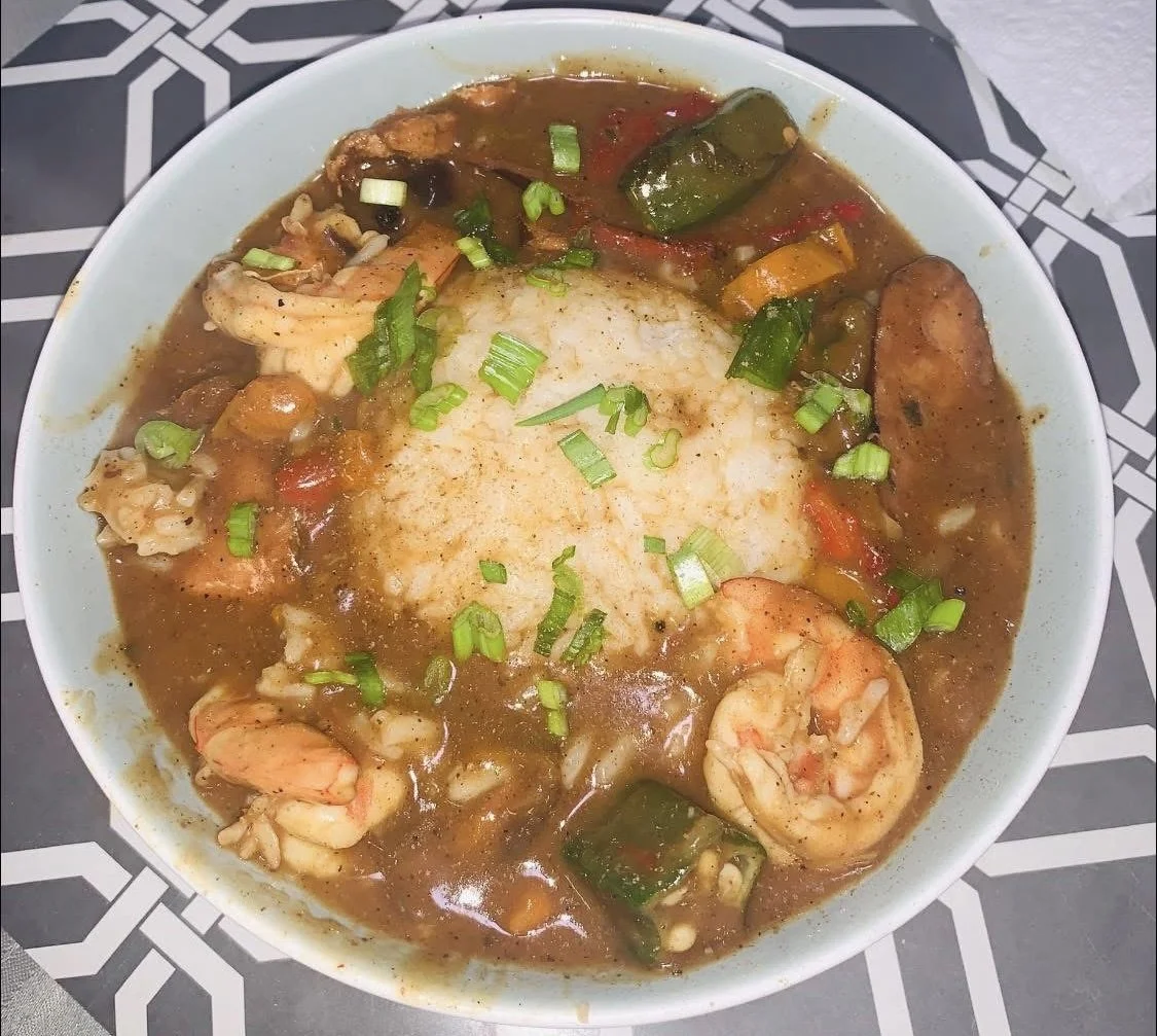 A bowl of shrimp and vegetable gumbo served over rice, garnished with chopped green onions.