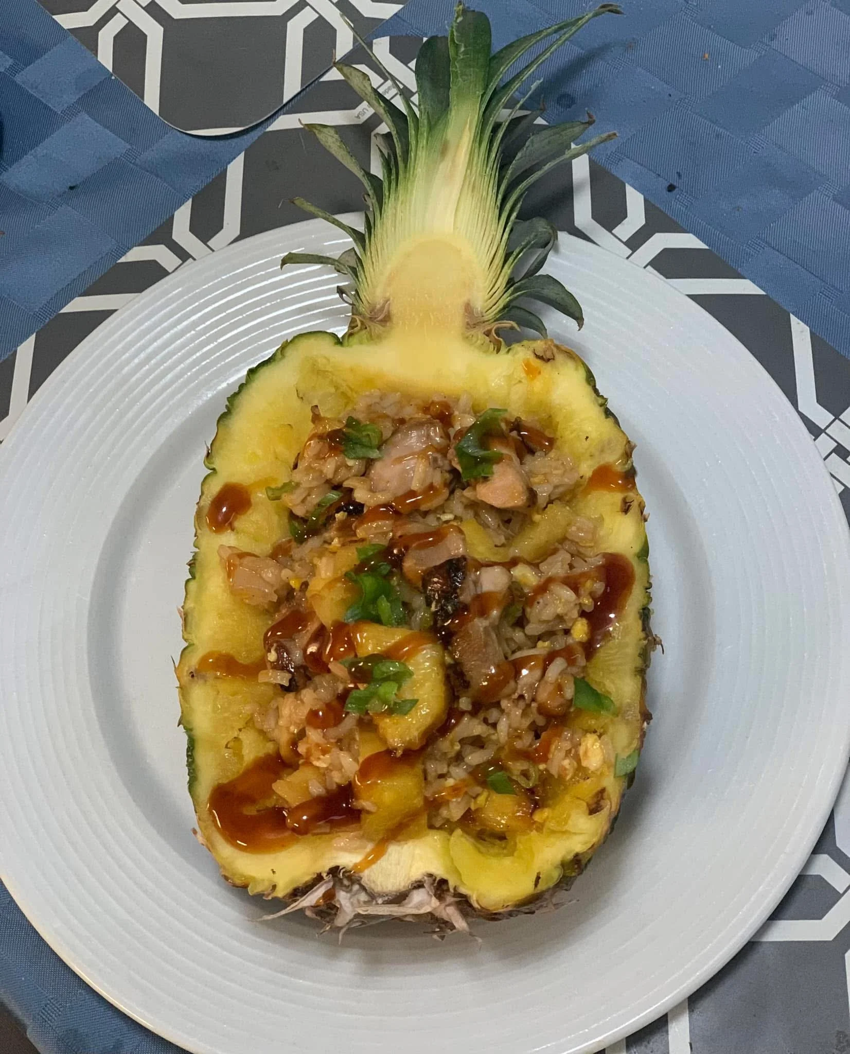 Hollowed pineapple filled with fried rice, topped with sauce, served on a white plate.