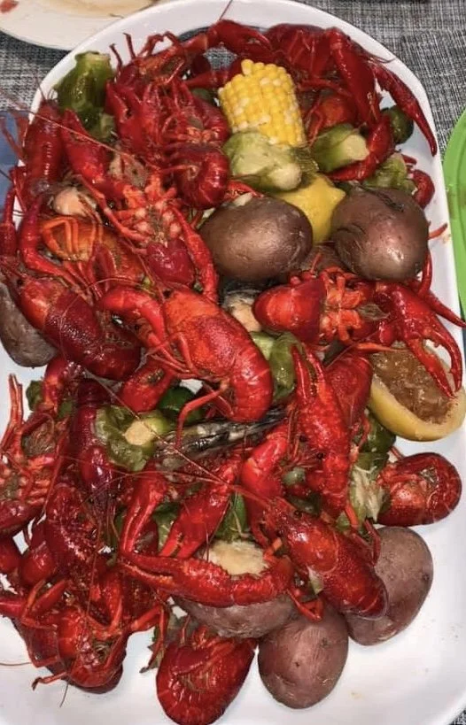 A white platter filled with cooked crawfish, yellow corn on the cob, brown potatoes, and green vegetables.