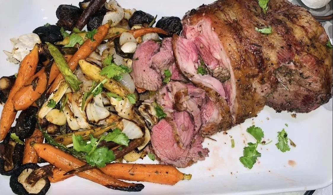 A plate of grilled sliced beef tenderloin served with roasted mixed vegetables, including carrots, onions, and mushrooms, garnished with fresh cilantro.