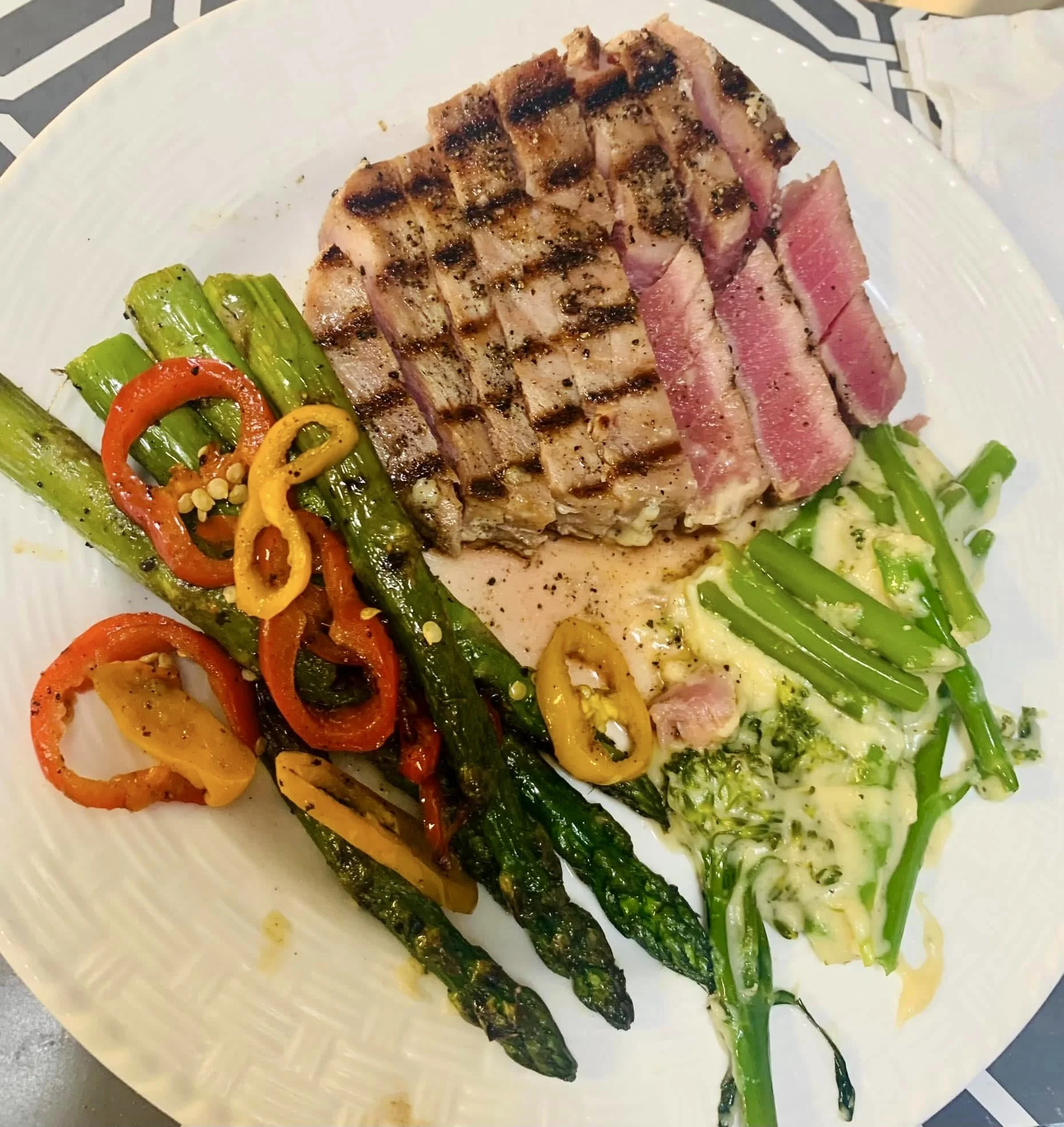 A white plate with grilled steak, green asparagus, and sautéed bell peppers, with some vegetables on the side.