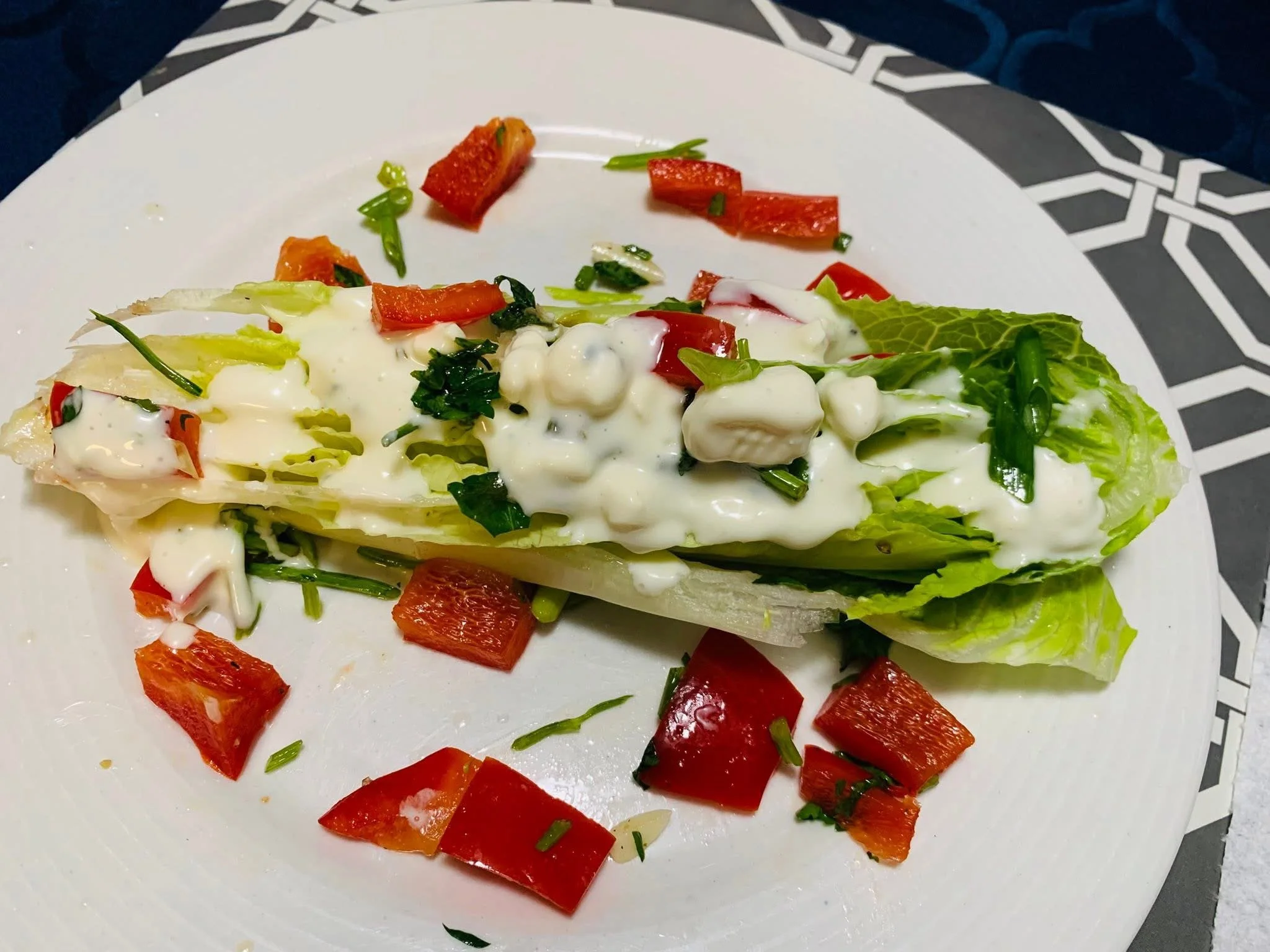 A plate of salad with chopped red bell peppers, green onions, lettuce, and a creamy white dressing.