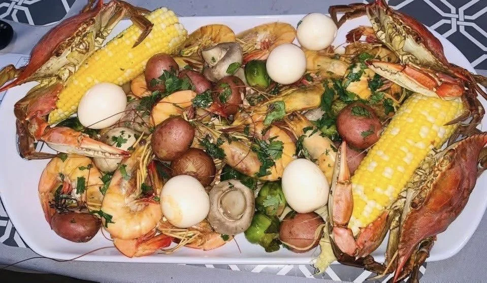 Seafood platter with lobster, shrimp, corn on the cob, boiled eggs, potatoes, and herbs.
