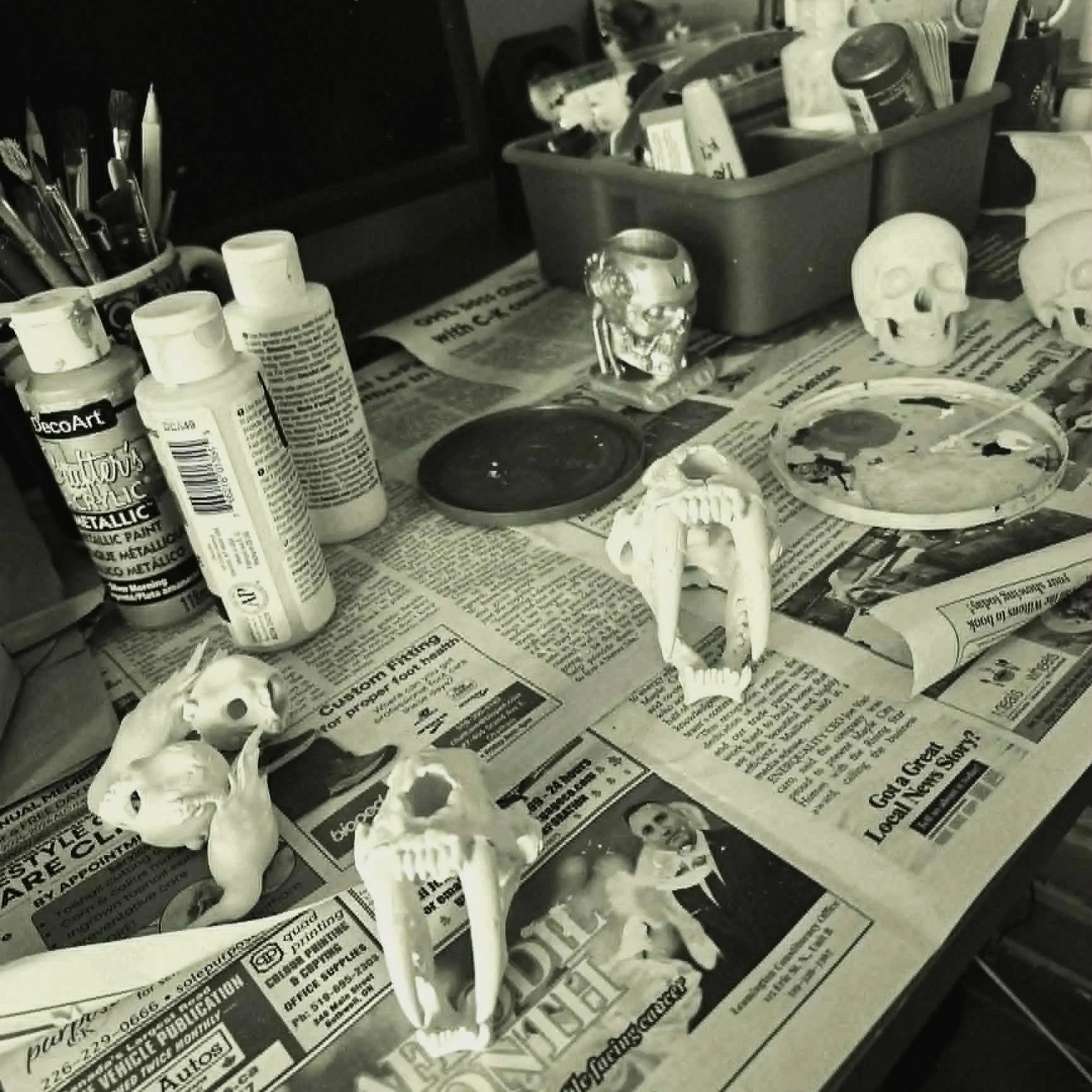 Various skull models and art supplies on a table covered with newspaper.