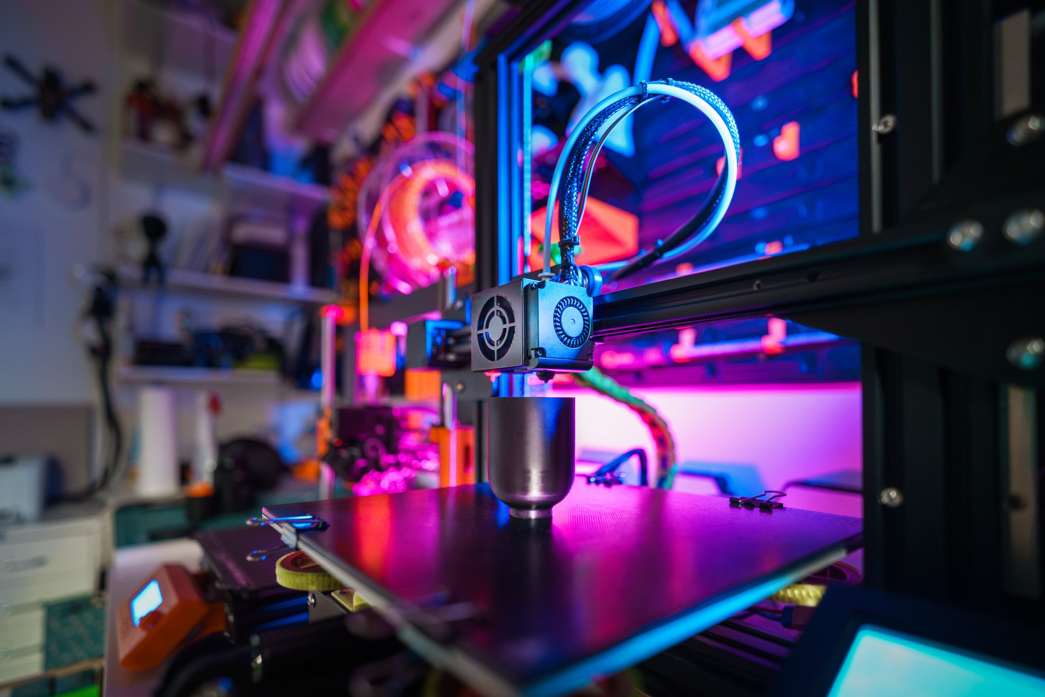 3D printer creating a colorful knit-textured design, illuminated by neon lights.