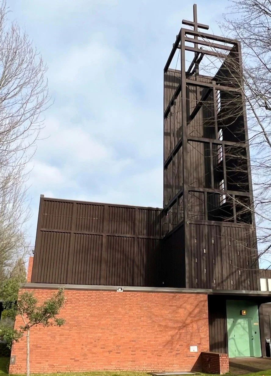 A modern building with a brick lower section and a dark wooden upper section, featuring a tall, open framework tower structure.