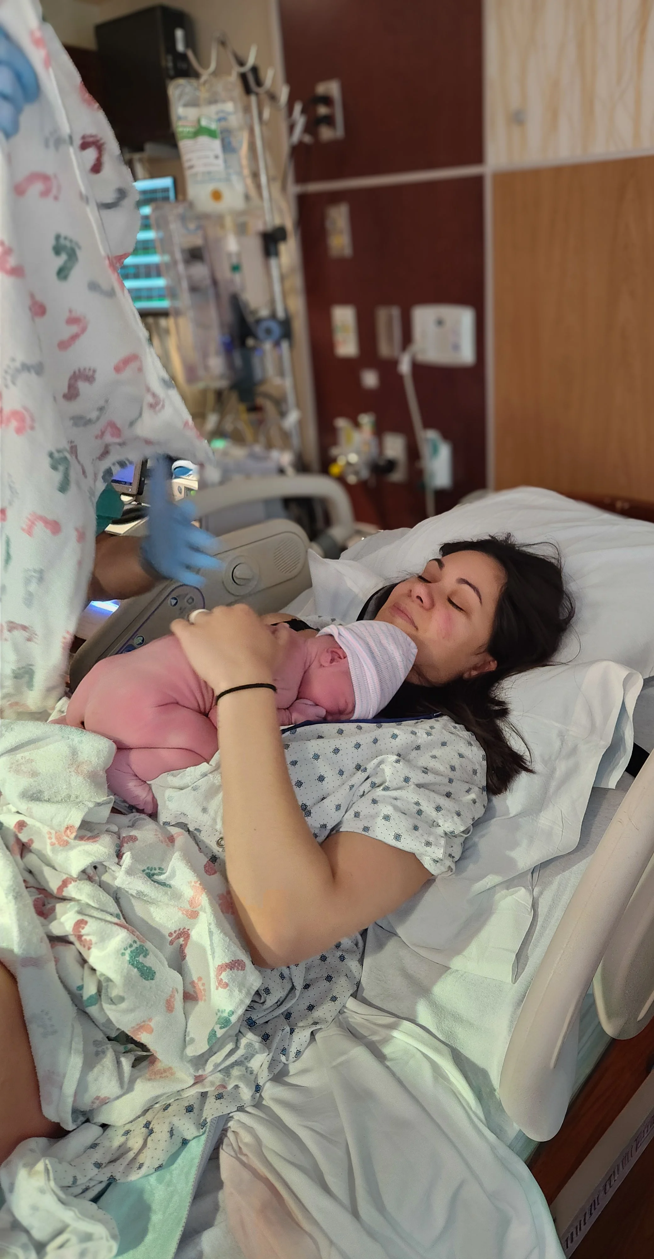 Woman lying in hospital bed holding newborn baby with hospital staff nearby.