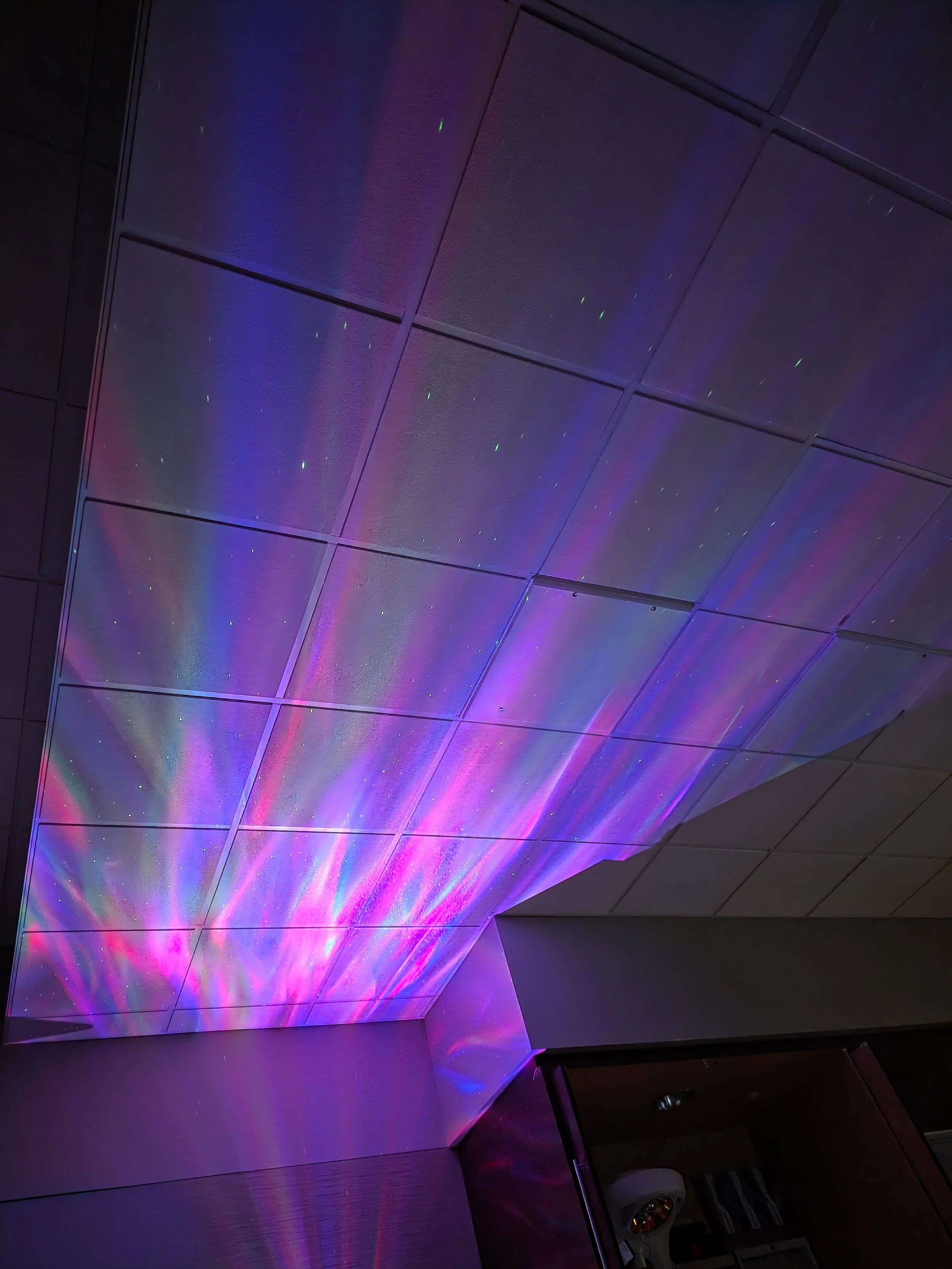 Ceiling with colorful laser lights projecting purple, blue, and pink reflections on the surface.