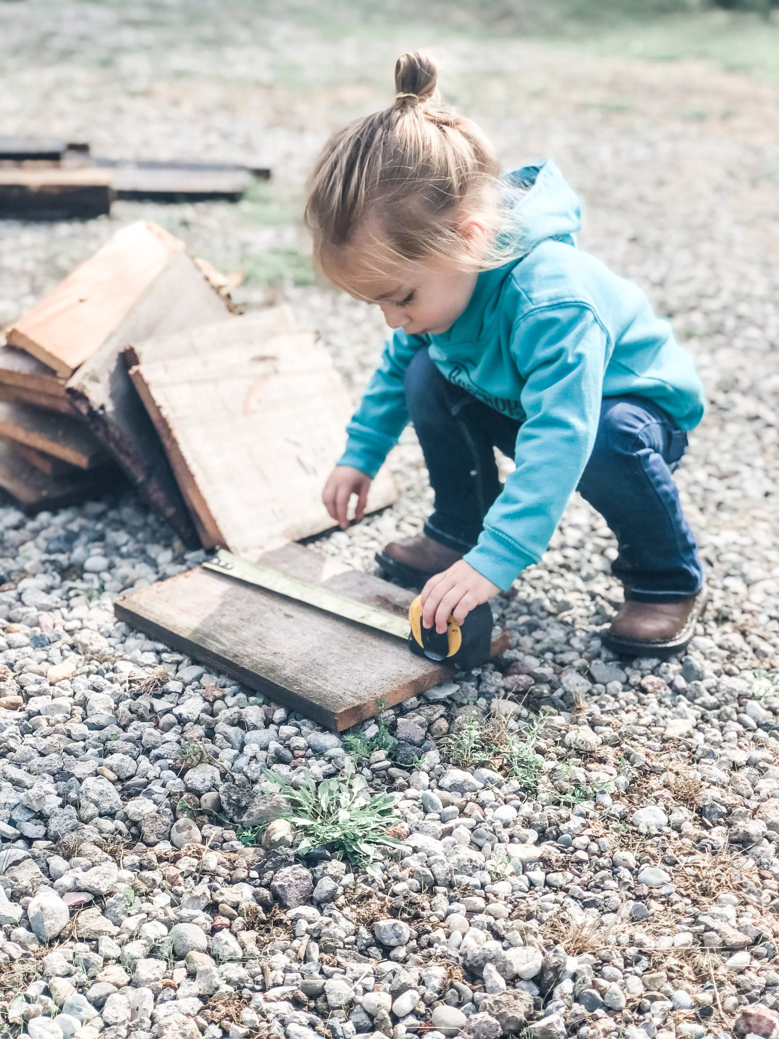A young girl measuring wood for an outdoor project at a rural home in Eatonville, Washington, reflecting hands-on homestead family life.
