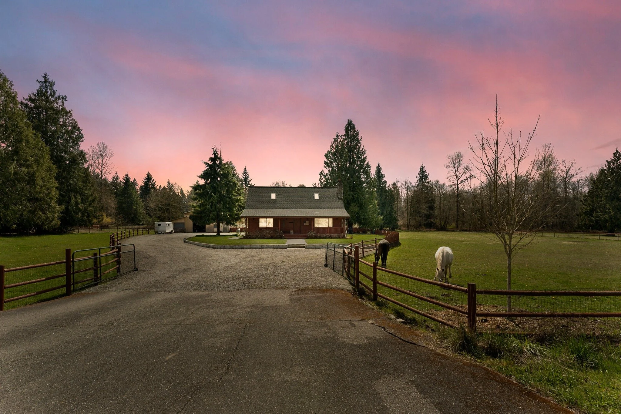Rural horse property at sunset in Eatonville, Washington, with grazing horses and a tree-lined driveway.