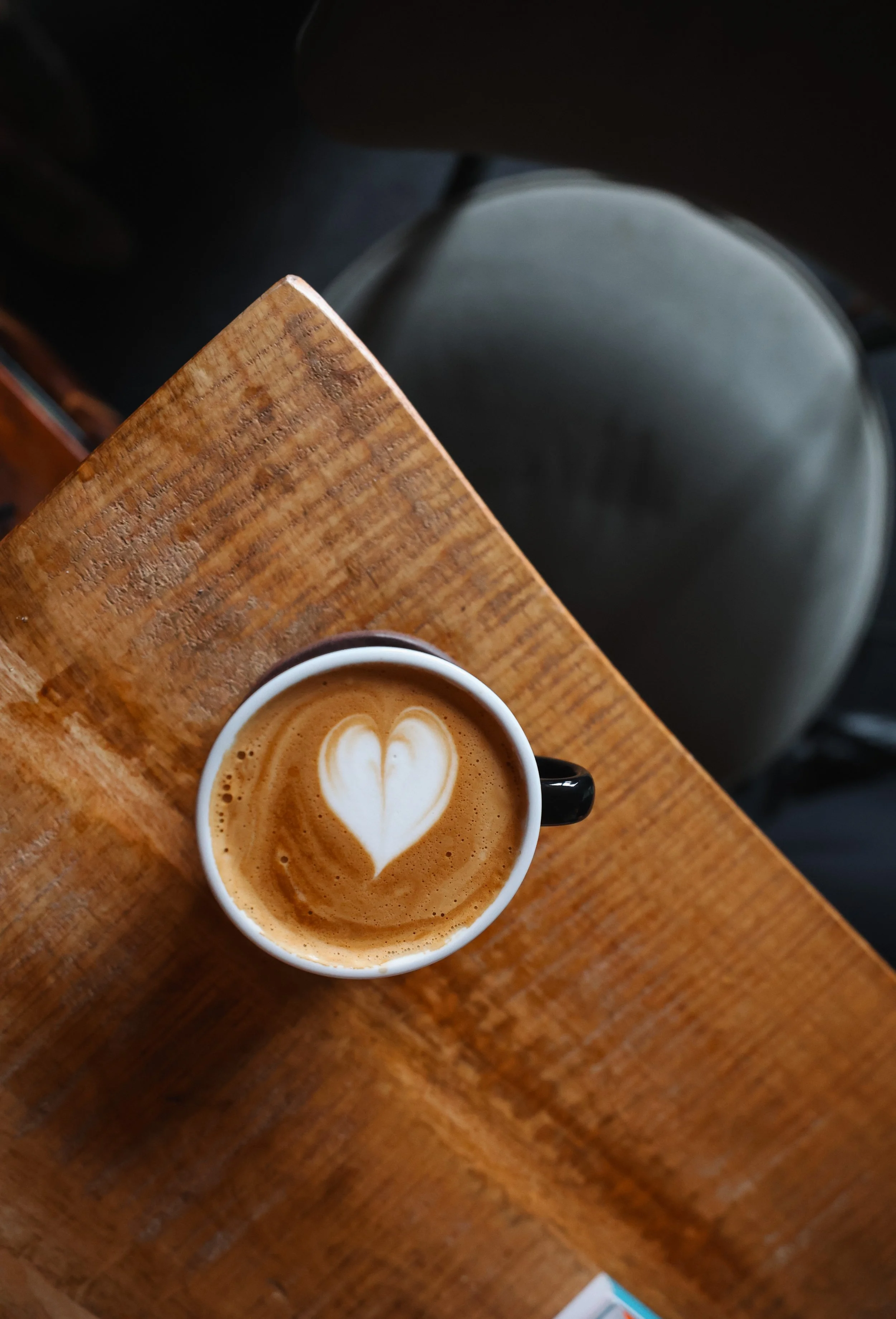 A cup of coffee with latte art in the shape of a heart, placed on a wooden table.