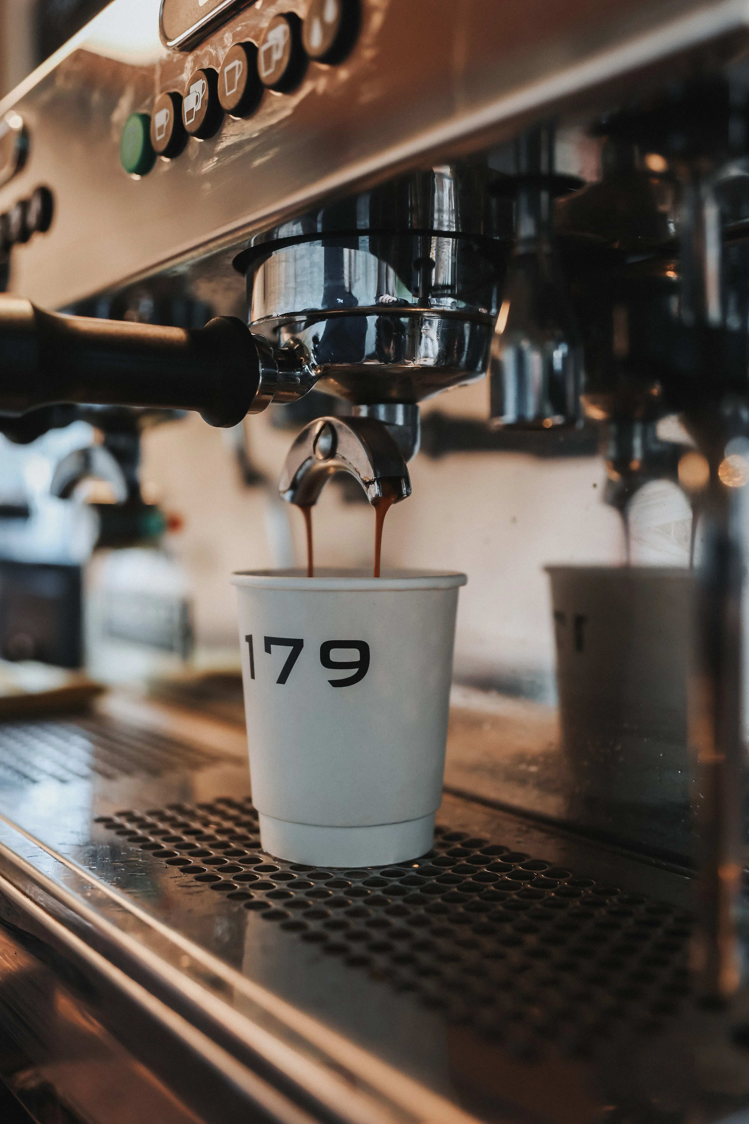 Coffee machine dispensing coffee into a white cup labeled with the number 179.