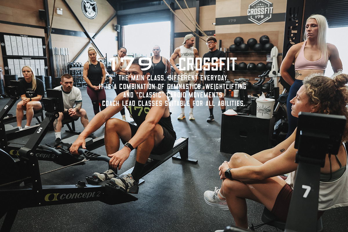 People working out and coaching in a crossfit gym with various equipment and a large window in the background.