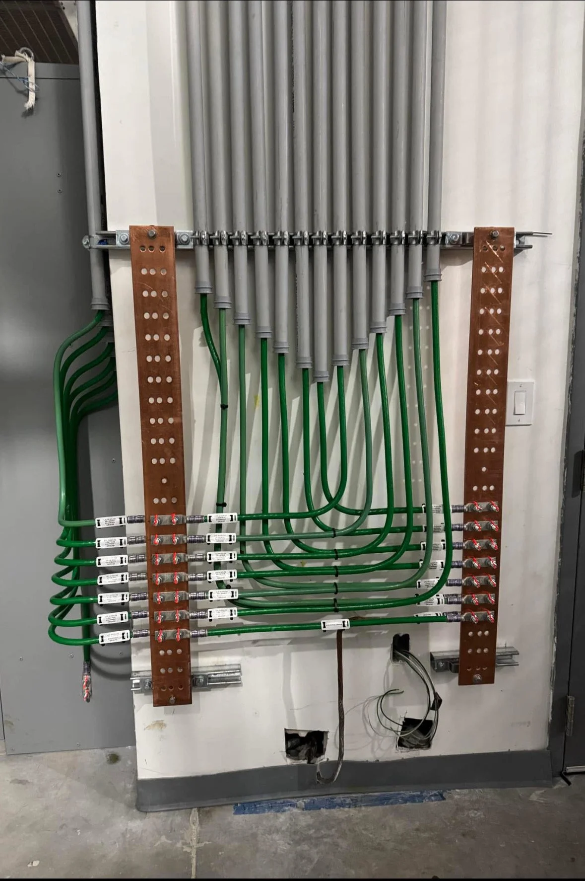 Electrical panel with organized wiring and green circuit tubes mounted on a white wall.