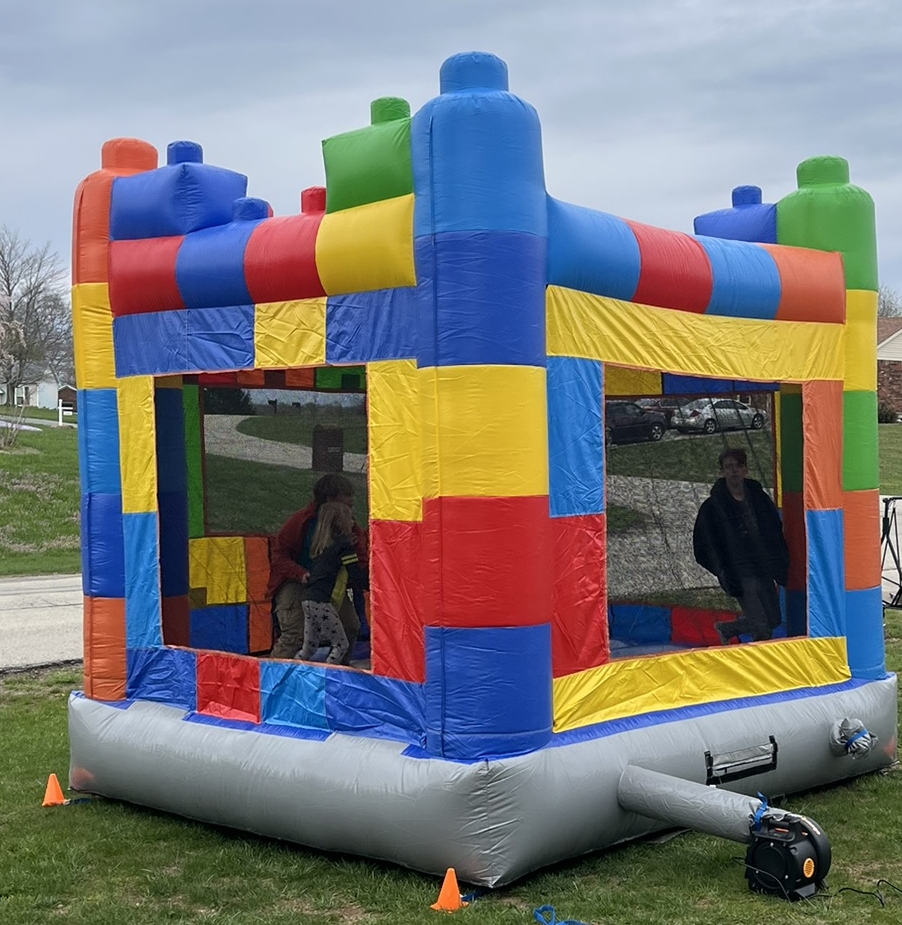 Colorful inflatable bounce house structure with children and an adult inside, set up outdoors on a grassy area.