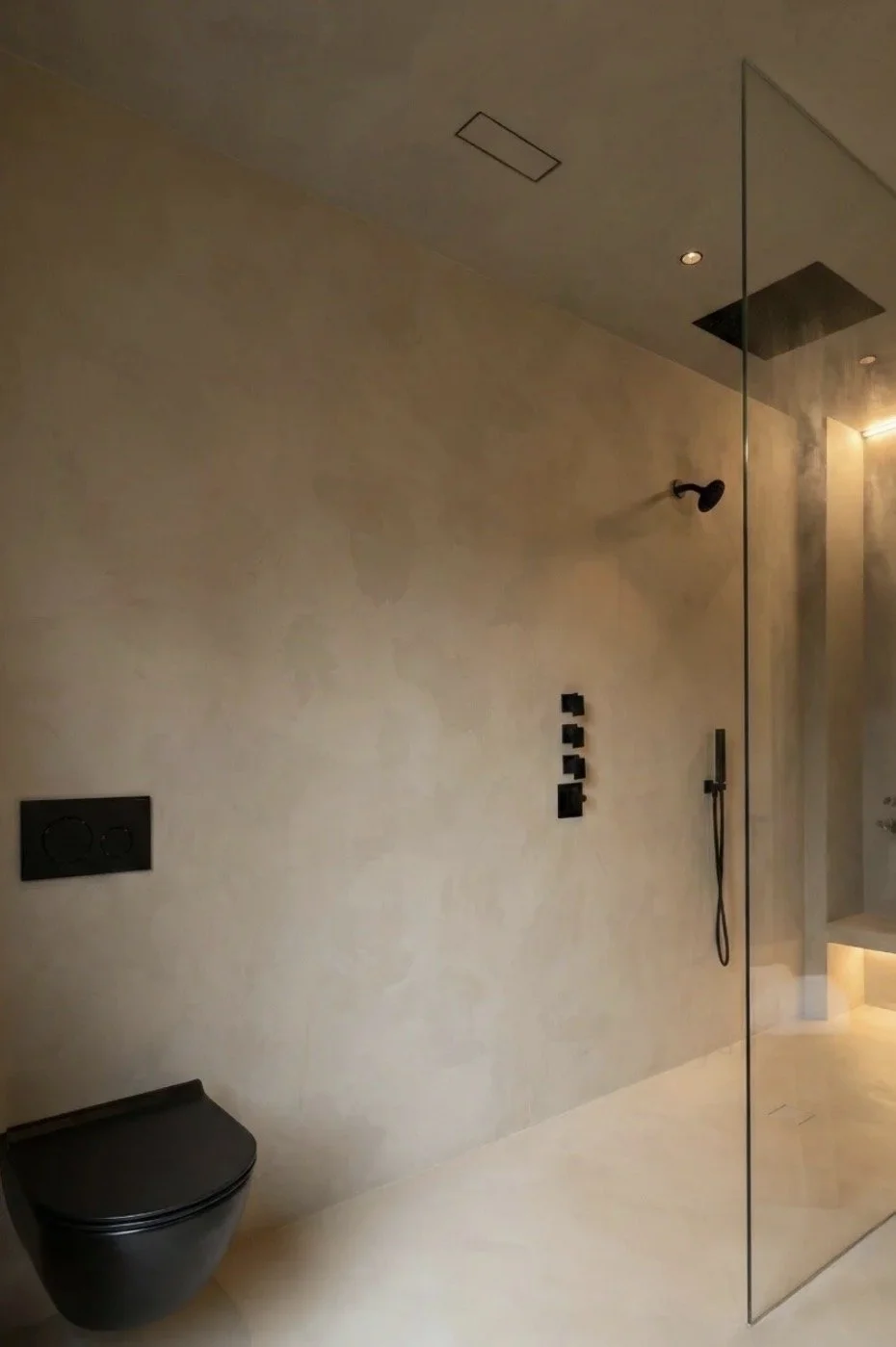 Moderne badeværelse med vægskyl toilet, bruser med glasvæg, sorte armaturer, downlights og minimalistisk design.