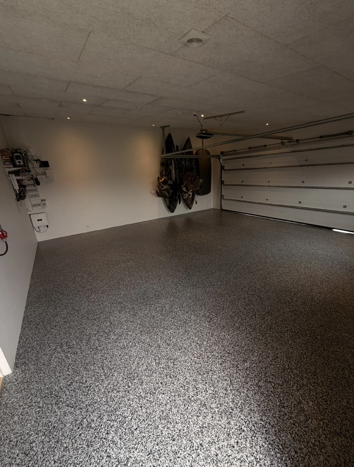 Et tomt garage med specklet gulv, en hvid væg med opbevaringshylder og board til skateboards.
