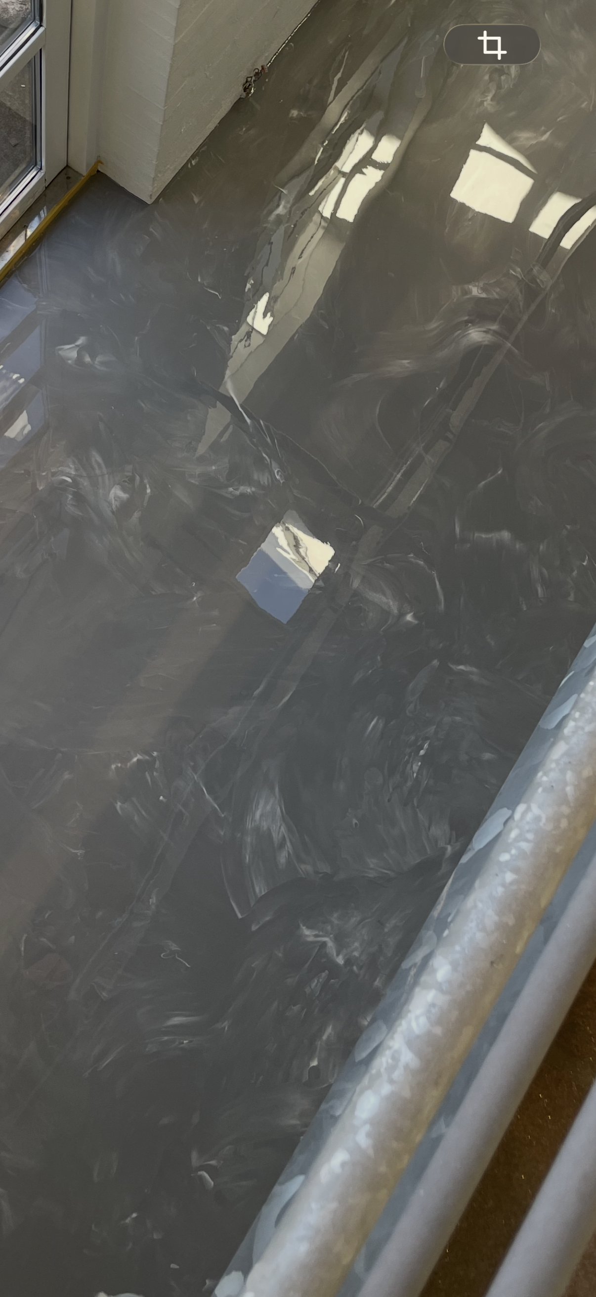 Udsigt af en byggeplads med ny beton- eller stengulv, der er blevet glattet ud. Der er bygningselementer og reflekser i overfladen.