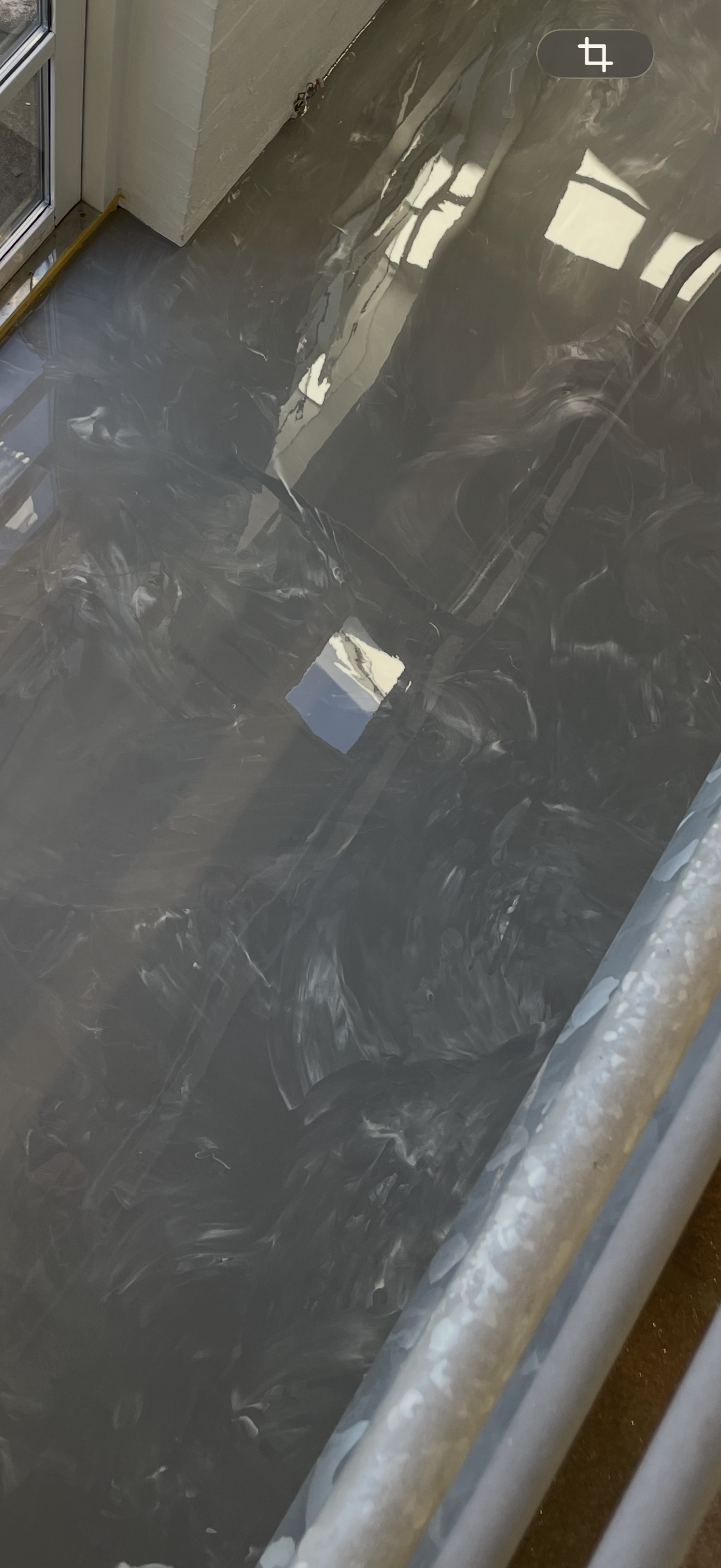 Sort, glat, reflekterende overflade, muligvis en poleret sten eller metallisk overflade, med refleksion af vinduer